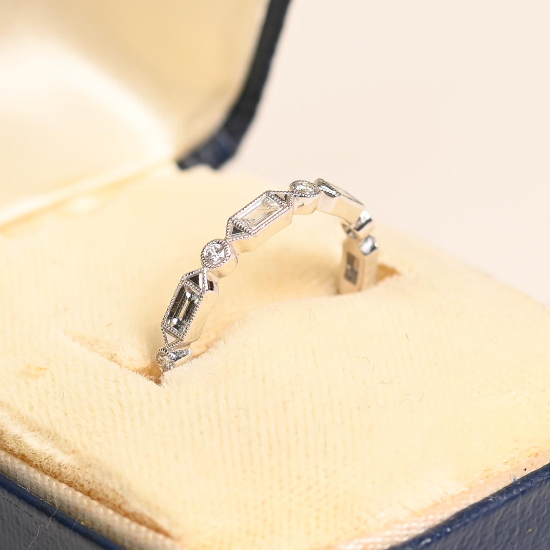 Questa squisita fascia geometrica per l'eternità mette in mostra un'impressionante combinazione di diamanti rotondi a taglio brillante e baguette, ciascuno meticolosamente incastonato in eleganti castoni. L'interazione di questi tagli di diamanti