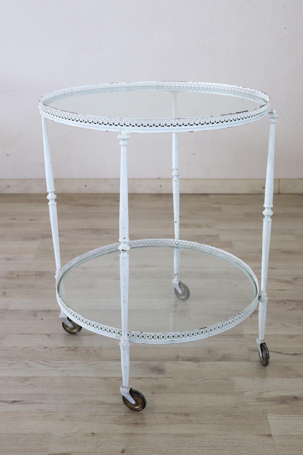 Rare 1980s Italian serving bar cart. Made of  white lacquered brass equipped with two round glass tops and brass wheels for convenient movement. The lacquering shows some signs of wear made deliberately to give a shabby chic decoration effect.