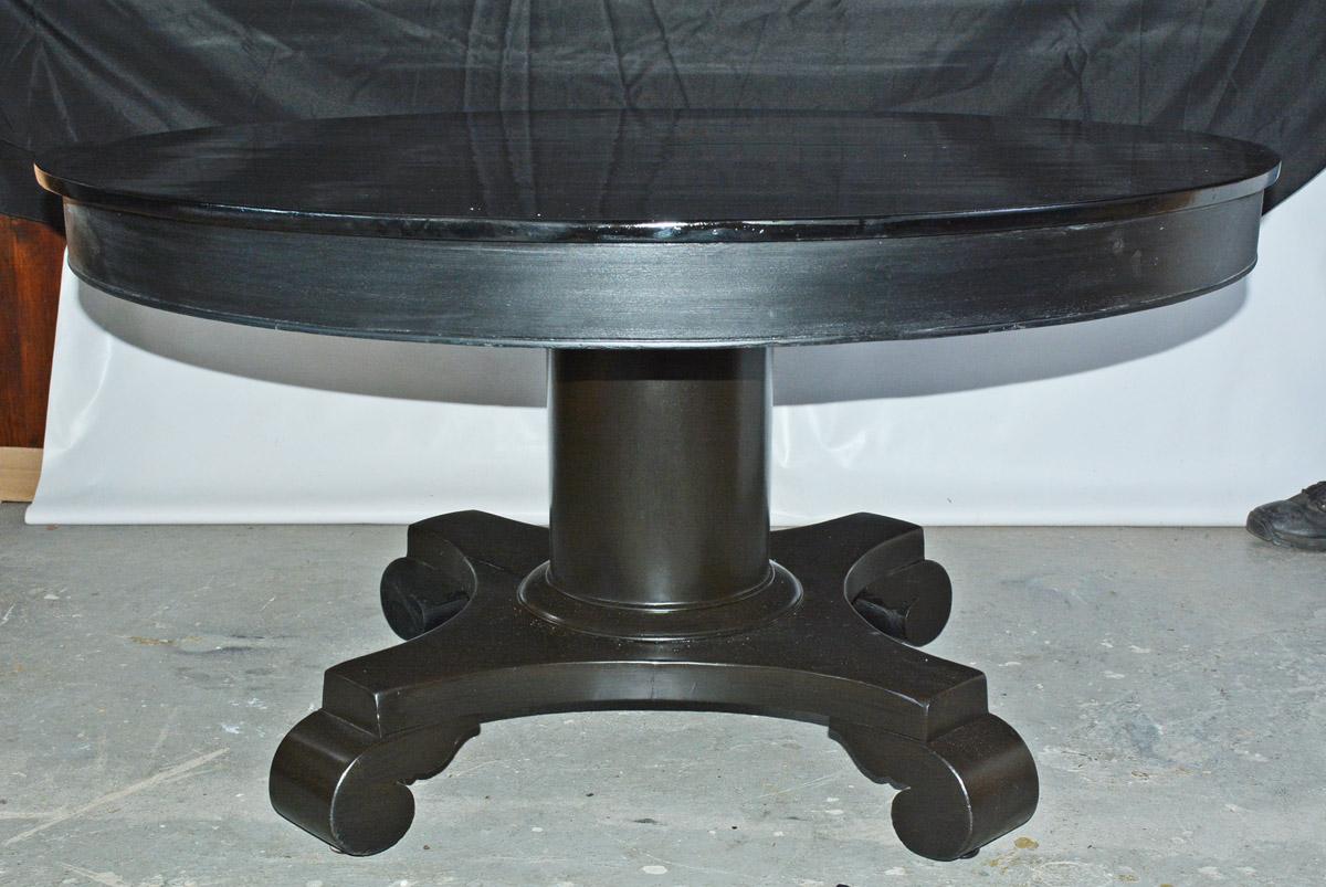 The round American Empire has four scrolled feet on wheels attached to a center pedestal. The table has been refinished in ebony black with a lacquered top. Although the table can be opened and extended. It does not have any leaves.