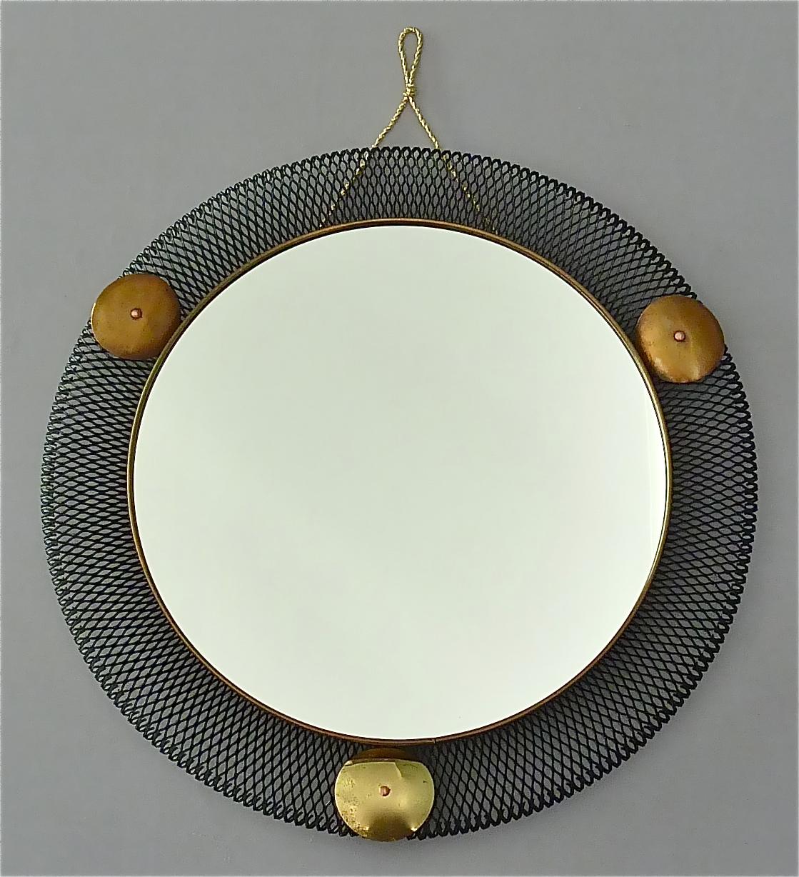 Round midcentury wall mirror which is made in the style of Jacques Biny, Mategot or Pierre Guariche, France or Italy around 1955. It is made of black lacquered or enameled stretched metal, lovely patinated brass details, mirror glass and a later