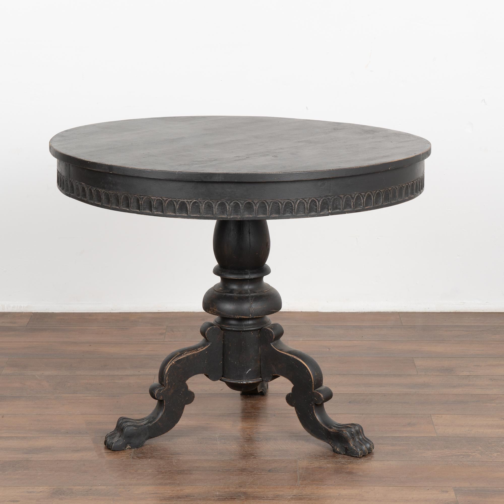 This round pine pedestal table has a carved skirt, turned pedestal base and decoratively carved tripod legs which were a traditional style in Sweden.
Restored, later professionally painted in layered shades of black and lightly distressed to fit the