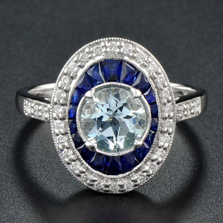 This stunning halo engagement ring has a refined Art Deco appeal. The oval round aquamarine is framed in French cut deep blue sapphire and further set with a border of diamonds with delicate, classic millgrain halo. The shoulders of the ring are
