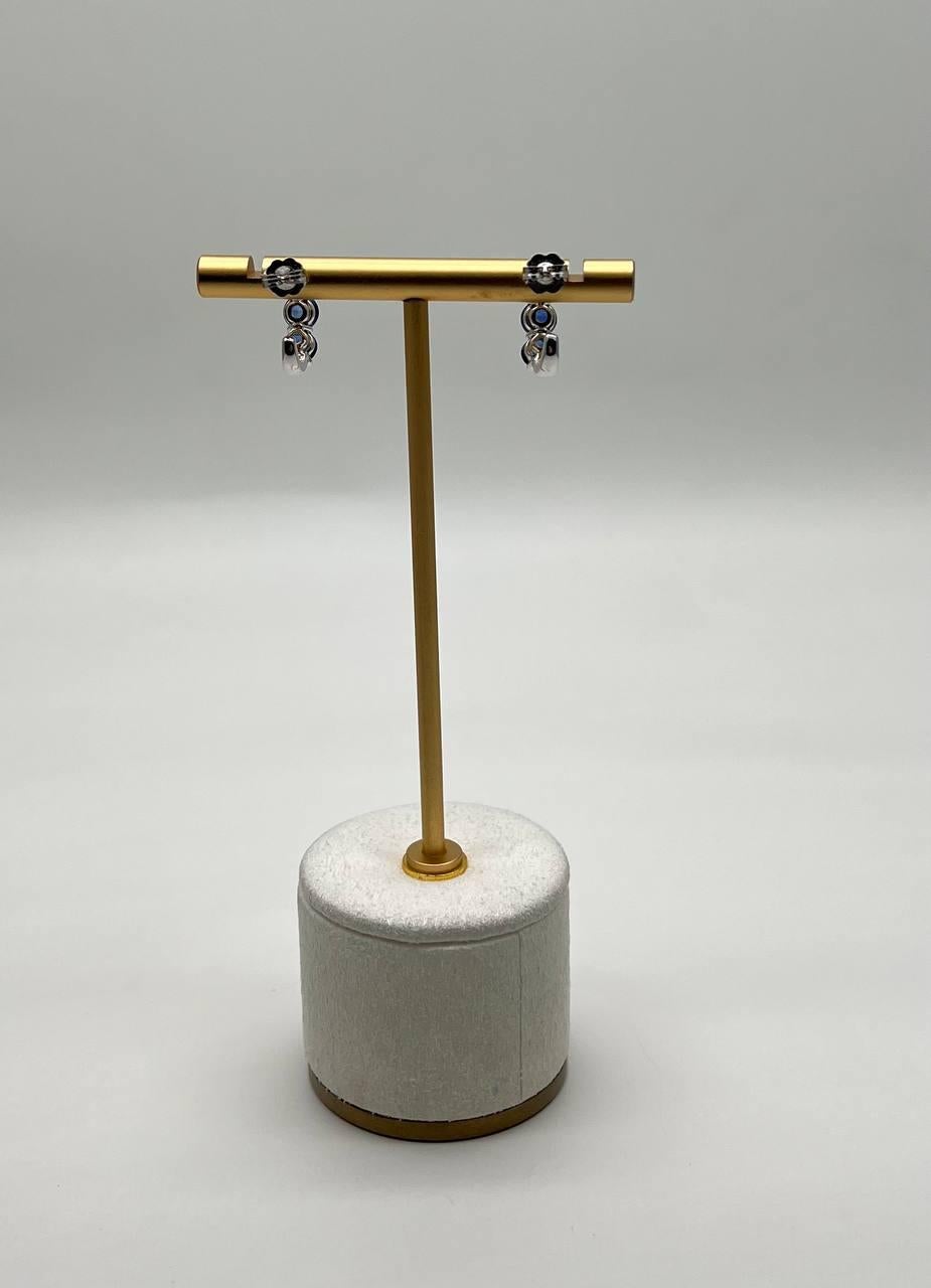 A sophisticated pair of earrings, featuring a sleek design with a series of dark, round blue sapphires. The earrings are elegantly displayed on a minimalist gold stand with a cylindrical base, showcasing their modern aesthetic. 14K White Gold. 4.27