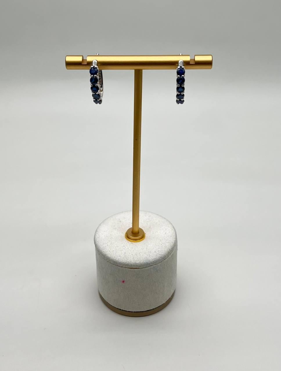 These sophisticated earrings each feature a series of deep blue sapphires set in a sleek, white gold hoop design.
The stones are arranged in a continuous line, creating a striking contrast against the polished white gold.
The design is both timeless