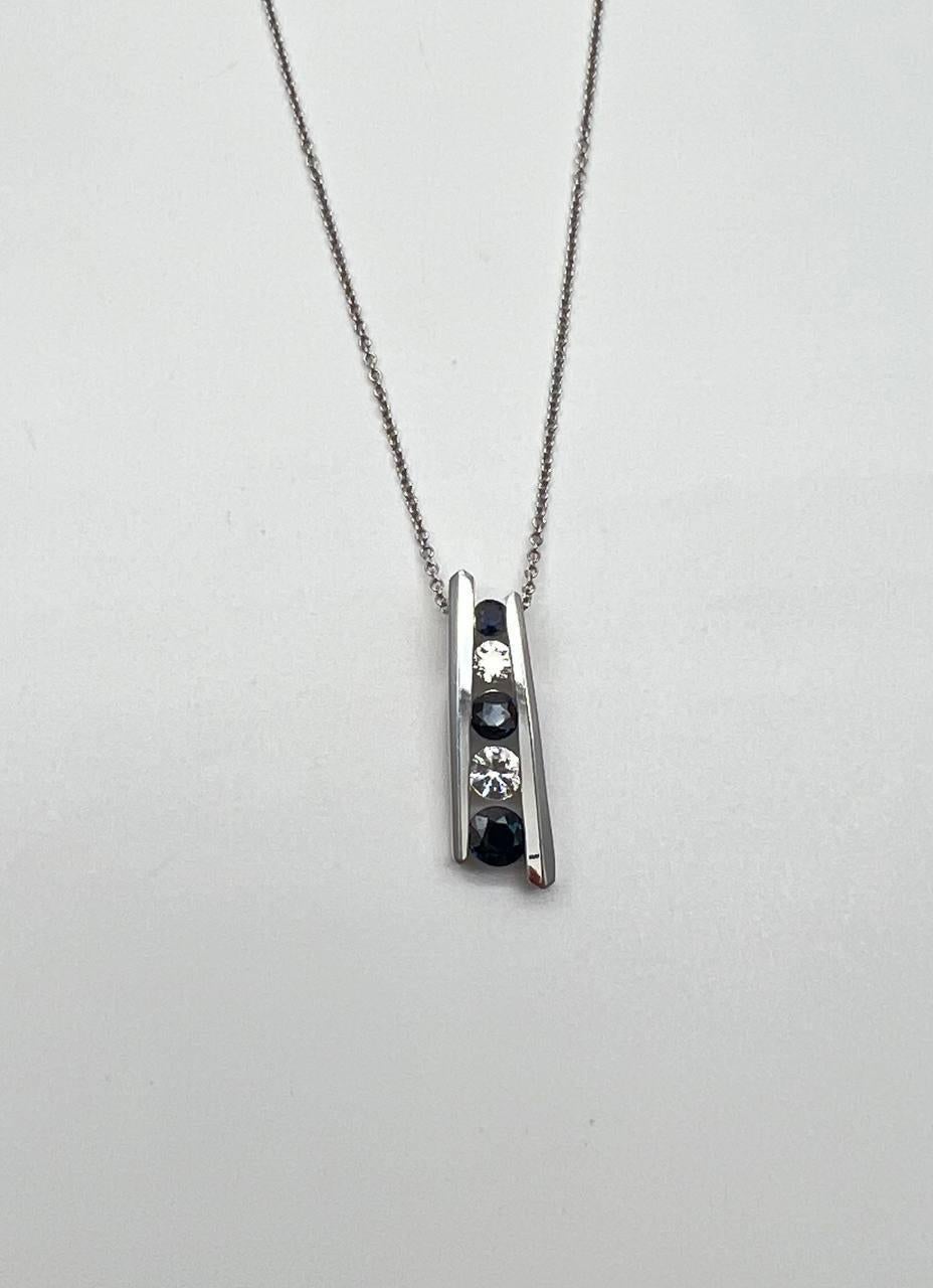 Experience the refined simplicity of this pendant necklace. This piece features a sleek, modern design with a vertical arrangement of alternating blue sapphires and white diamonds set in a polished metal frame. The pendant hangs elegantly from a
