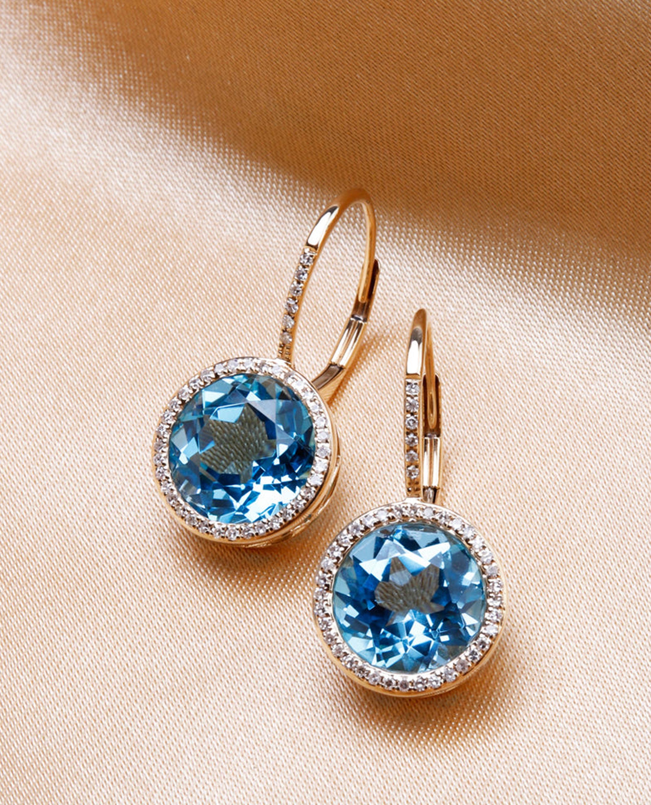 Boucles d'oreilles halo en or jaune 14K avec deux topazes bleues rondes pesant 9,50 carats au total et 84 diamants ronds pesant 0,20 carat au total.

Les boucles d'oreilles ont des dos à levier avec des diamants sertis sur le devant ainsi qu'autour