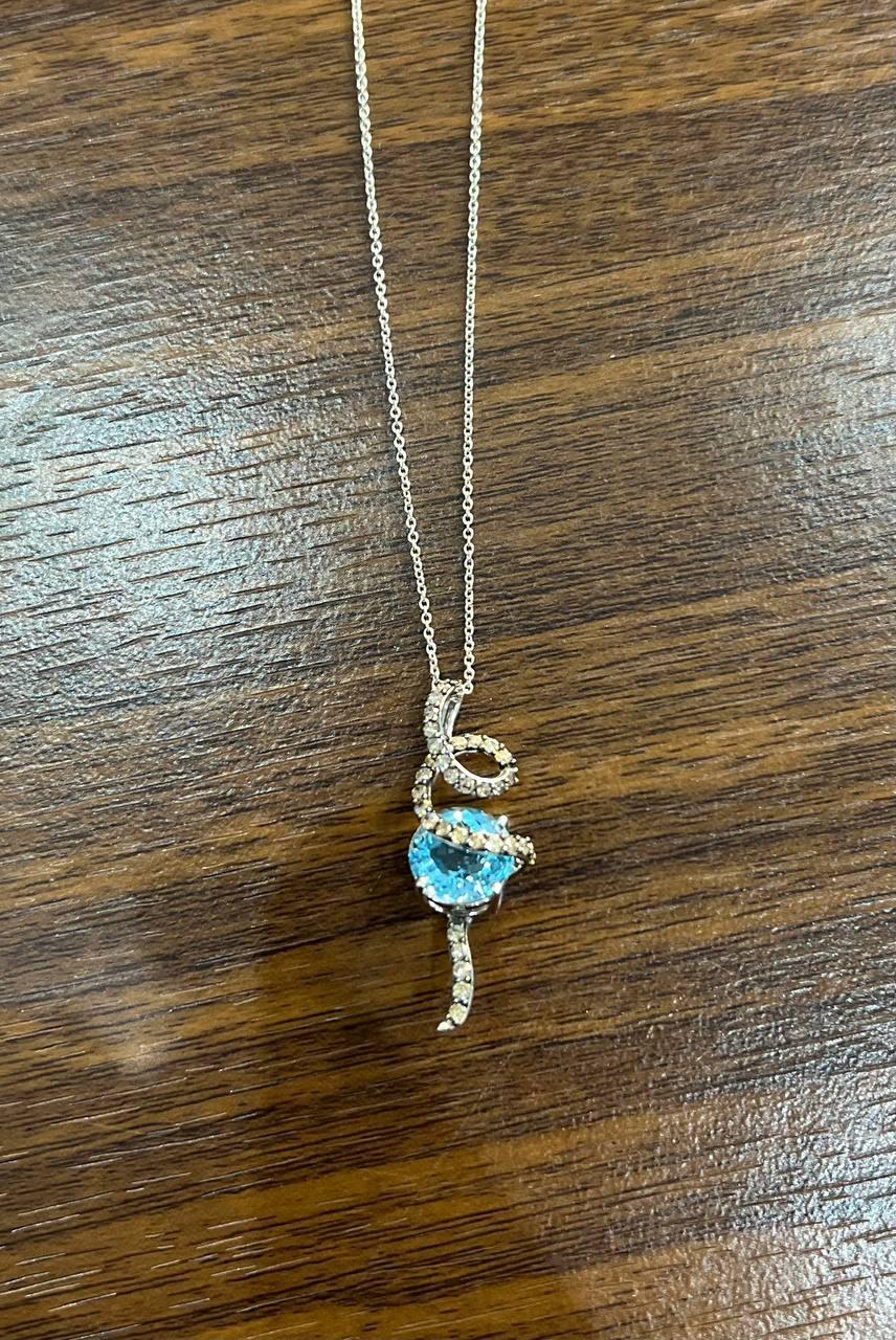 A delicate necklace featuring a pendant crafted in 14K White Gold, adorned with sparkling champagne diamonds. The pendant showcases a whimsical design with a central blue topaz, embraced by a swirl of smaller diamonds, forming a playful tail-like