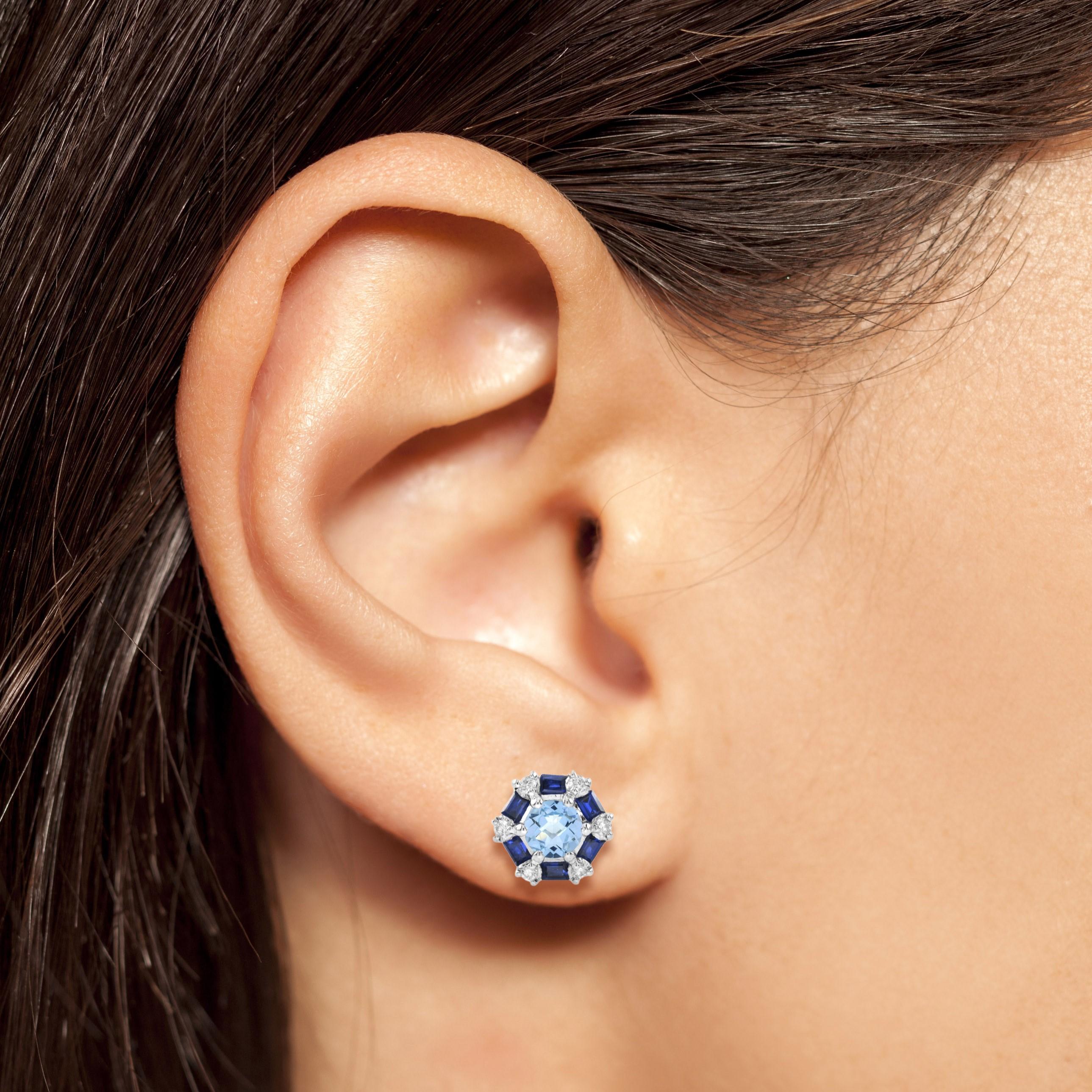 Ces ravissantes boucles d'oreilles en topaze bleue, saphir et diamant présentent un design Art déco et sont centrées sur une topaze bleue de taille ronde dans une monture à six griffes. Le centre est entouré de six saphirs bleus taillés en baguette