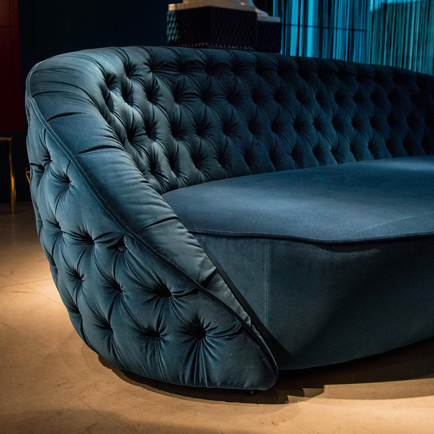 This timeless and sophisticated sofa is distinctive for is enveloping shape, created by the back and armrests. Its sinuous silhouette is elegantly upholstered with a rich blue shade of velvet that boasts a quilted texture on the backrest. The