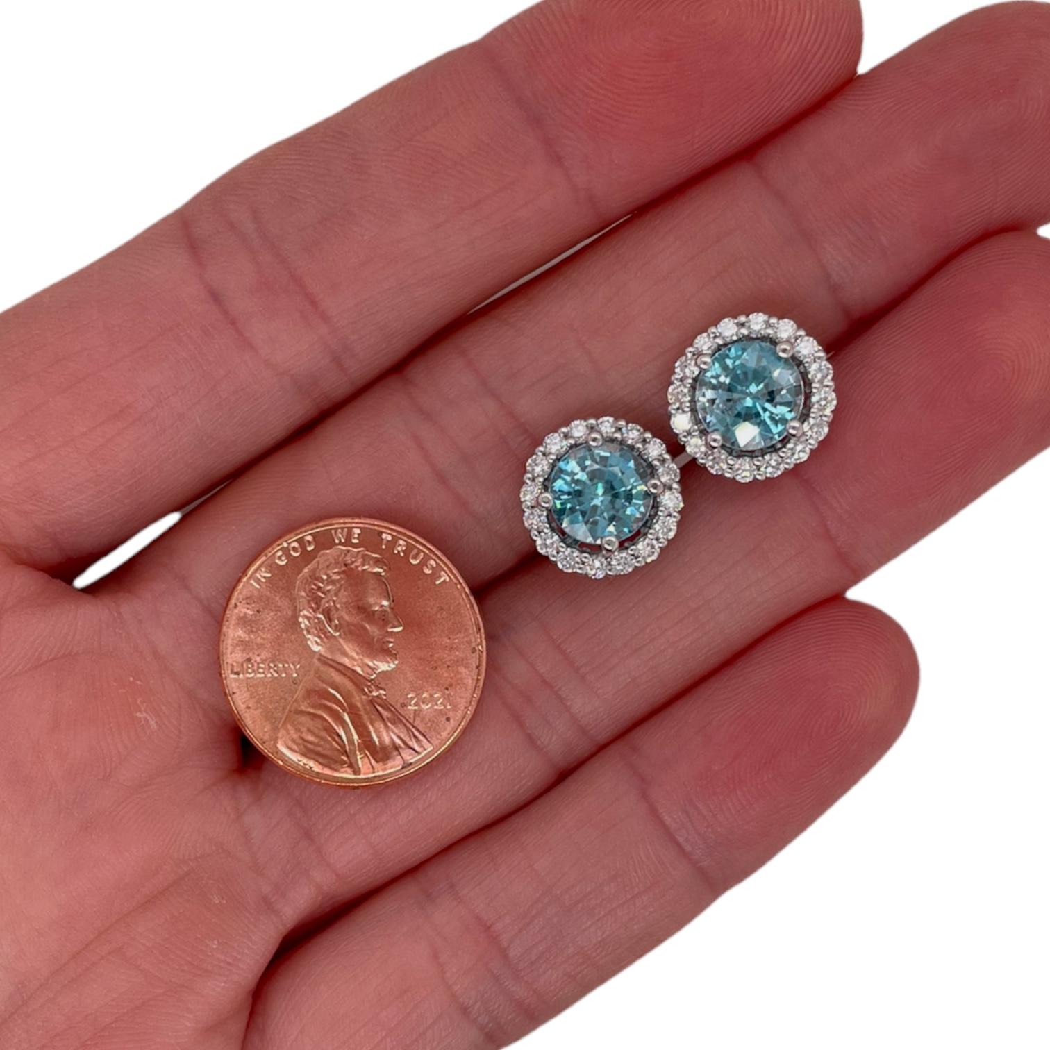 Classic diamond halo & blue zircon stud earrings in 18k white gold. Earrings contain 2 round brilliant blue zircons 3.81tcw, measuring approximately 6.9mm and round brilliant diamonds surrounding 0.55tcw. Diamonds are near colorless and SI1 in