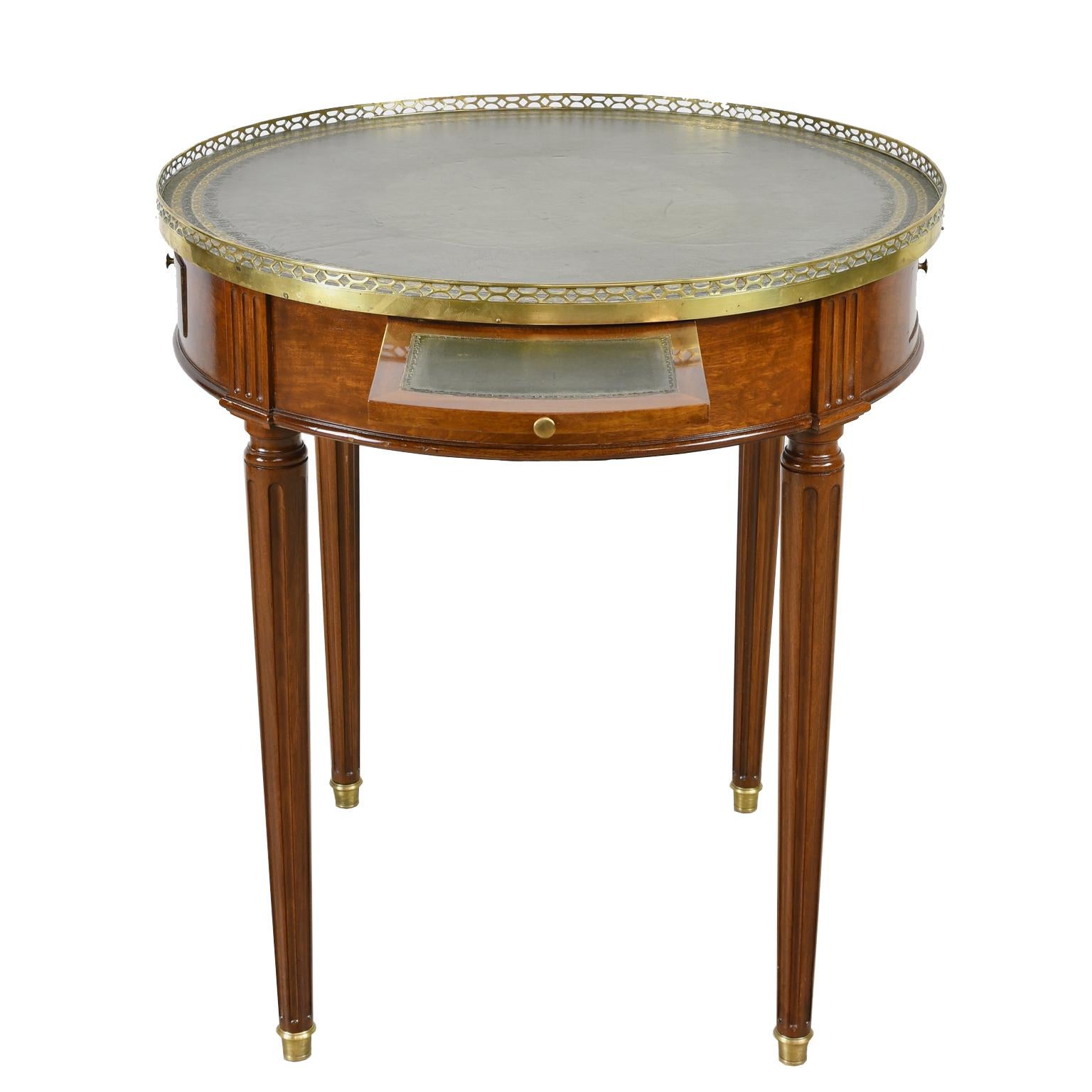 A French Bouillotte table in African mahogany in the Directoire style with dark green leather top with gilded and embossed border, and brass gallery. Round tabletop rests on turned and reeded legs with brass sabots and offers two drawers and two