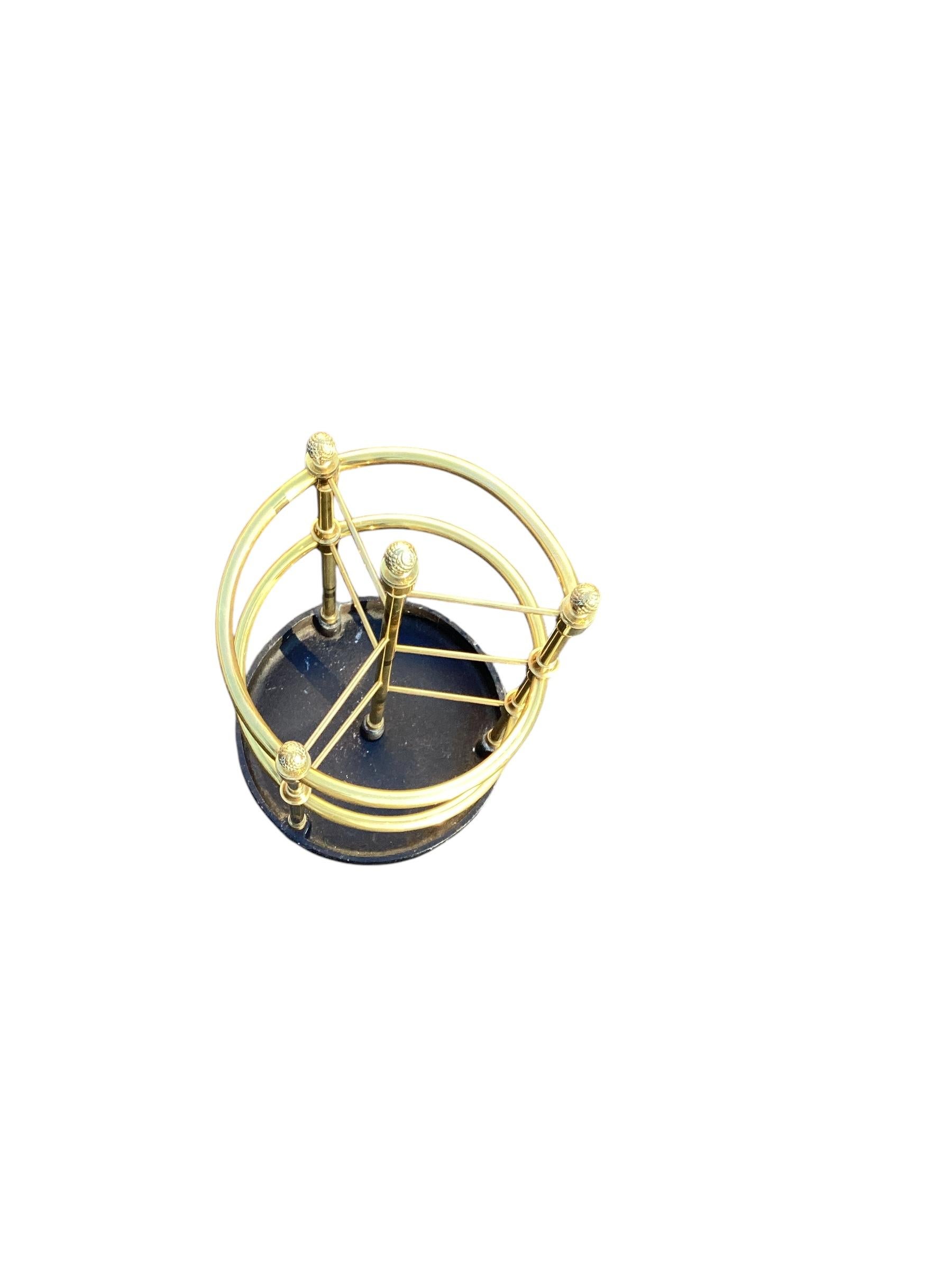 A circular brass and heavy cast iron umbrella stand. The circular design features brass tubular columns that terminate in brass pine cone finials.
