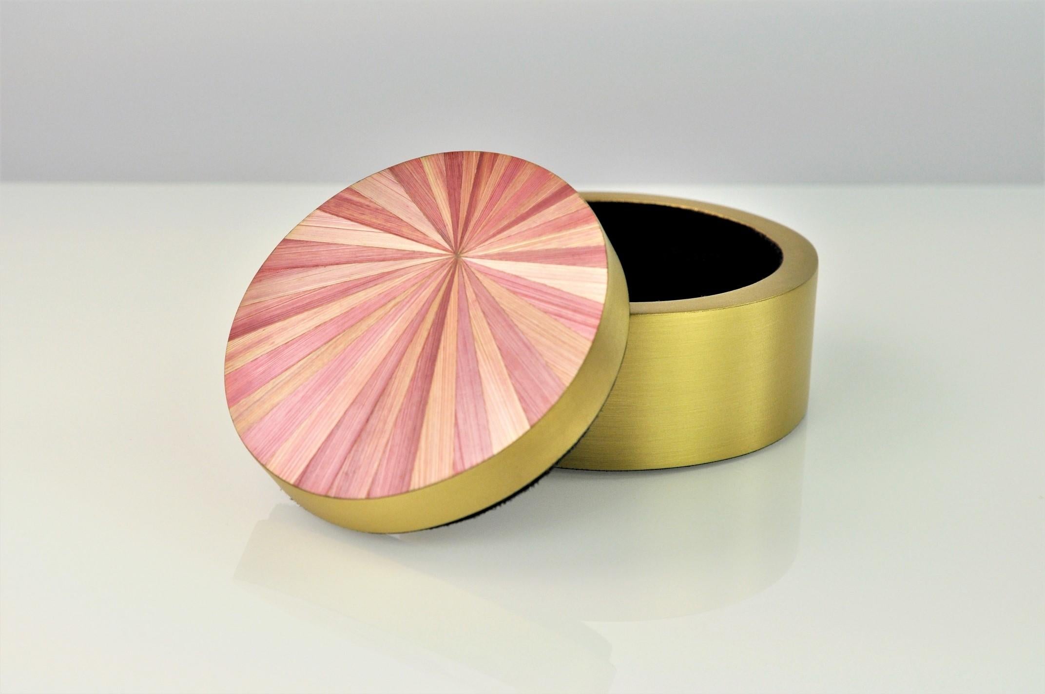 This lovely round brass box is made of brushed brass with a lid covered of straw marquetry. 
The radial design of the straw reminds the great Art Deco period while the elegant pink color contrasts perfectly with the gold brass.
The base has a