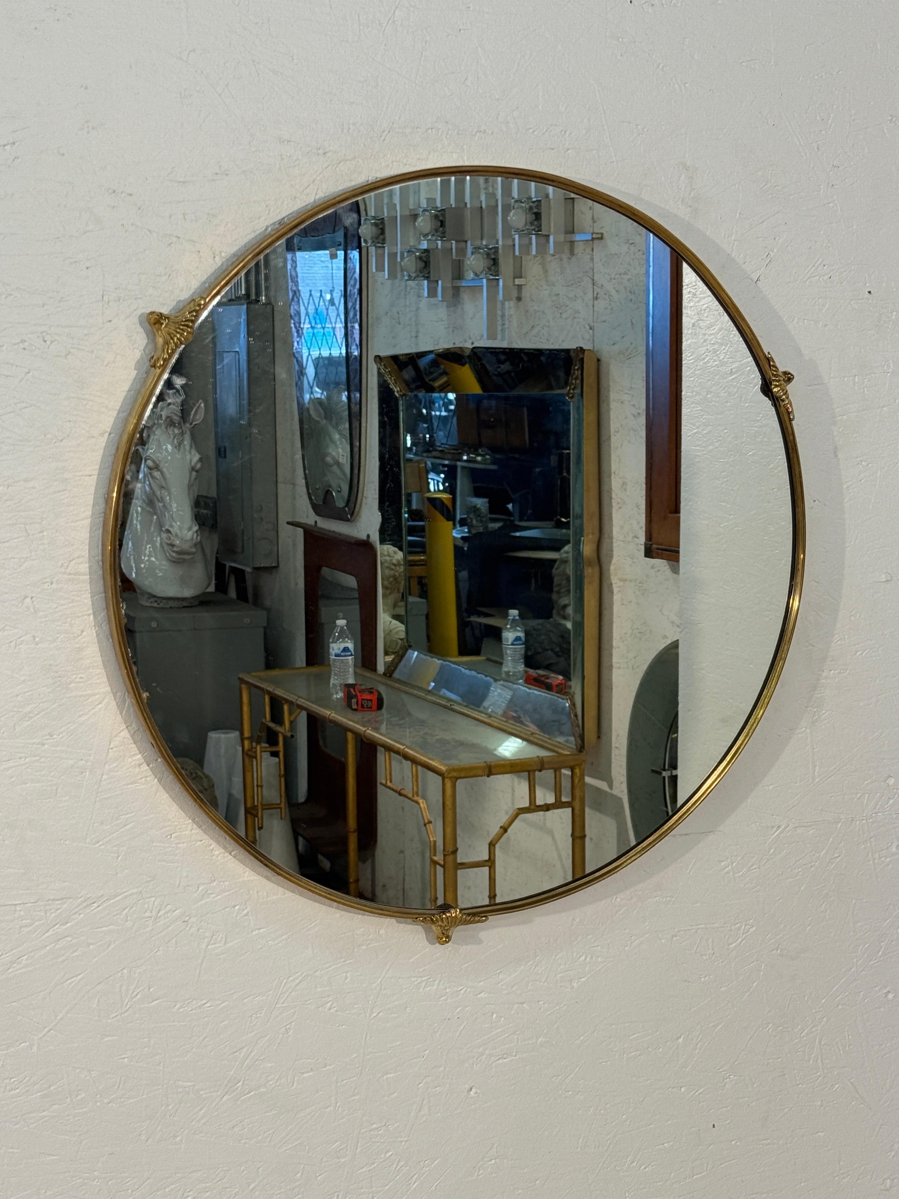 Miroir mural rond doté d'un cadre fin en laiton accentué par de petites montures décoratives en haut, sur les côtés et en bas. Sa forme circulaire minimaliste est rehaussée par de subtils détails classiques, ce qui lui confère un caractère raffiné