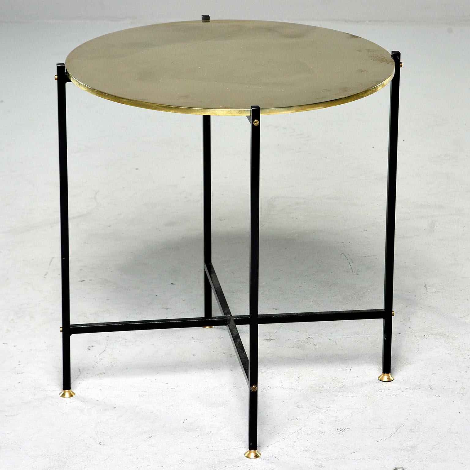 Contemporary side table found in Italy has round, polished brass top with slender black iron base with X-form stretcher and brass feet. Two available at time of this posting. Sold and priced individually.