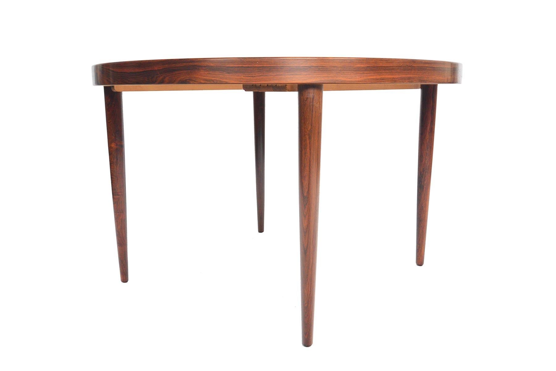 This beautifully simple round dining table was designed by Kai Kristiansen in the 1960s. Bookmatched Brazilian rosewood wood grain is banded with a clean and simple line. Table extends to hold an additional leaf and can comfortably seat four to six
