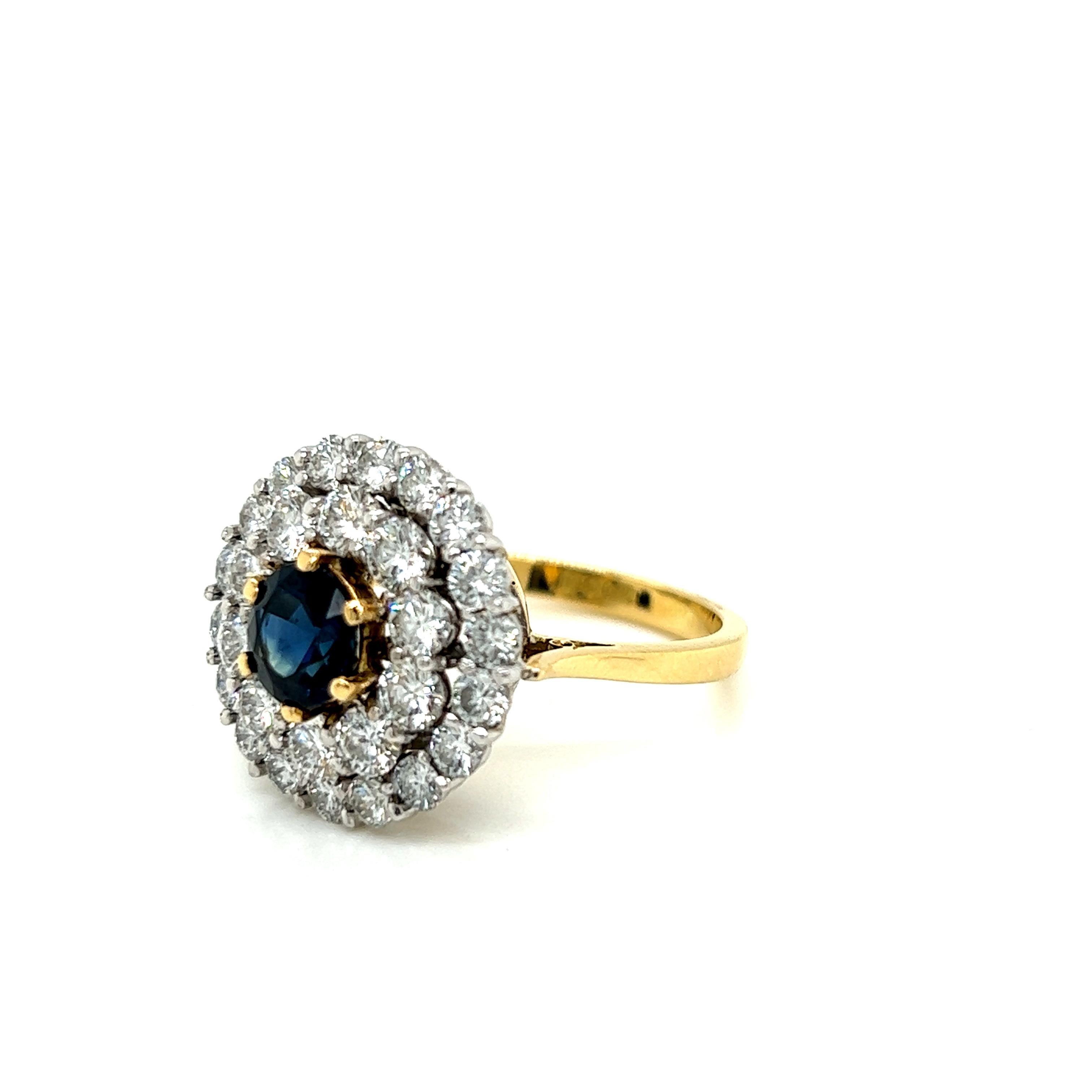 This magnificent ring features a 1.39 carat Round Brilliant Blue Sapphire at its centre, surrounded by 2.48 carats of Round Brilliant Diamonds on an 18K Yellow Gold Ring. The diamonds are set in 18K White Gold, and their arrangement gives the effect