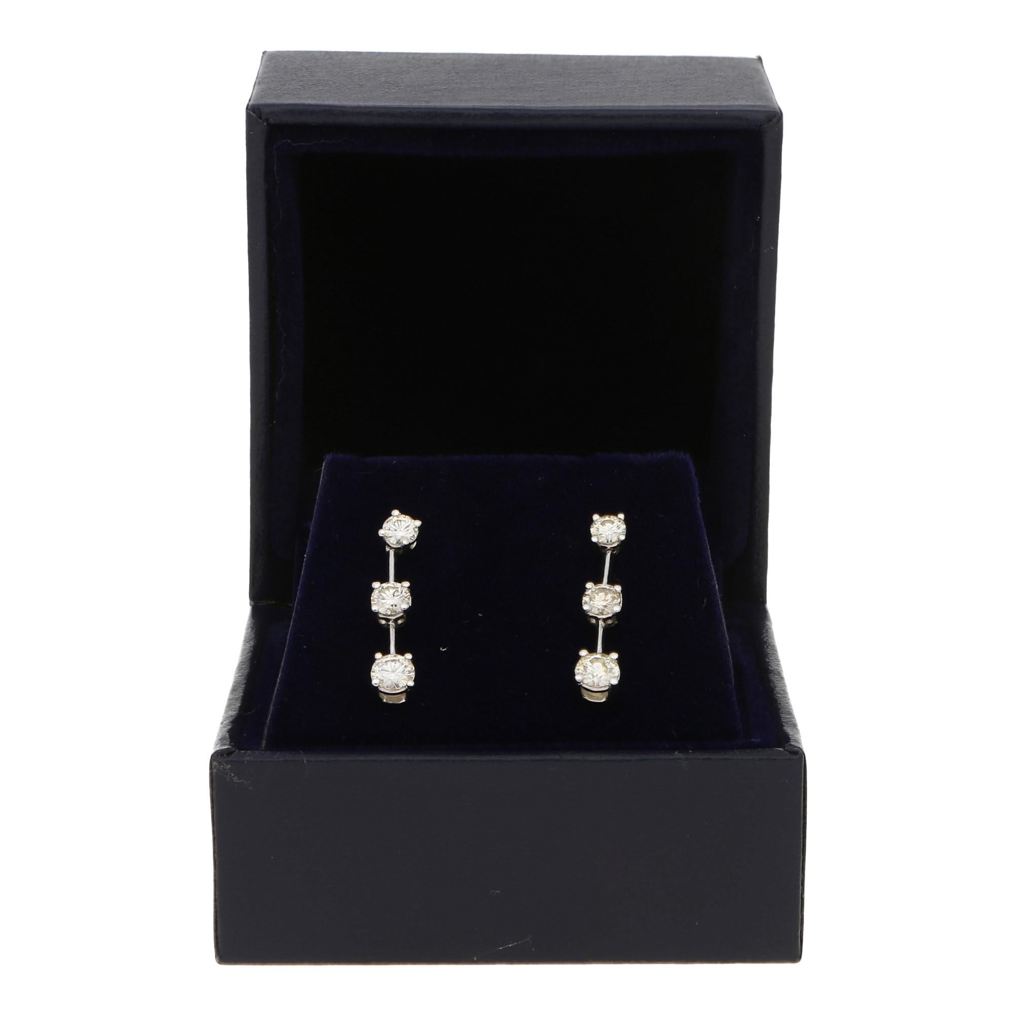 The total diamond weight is approximately 1.03 carats, J/K color and SI clarity.

An elegant pair of diamond station earrings in 18-karat white gold. 
Each earring is designed as a sequence of three round brilliant-cut diamonds claw-set in open-back