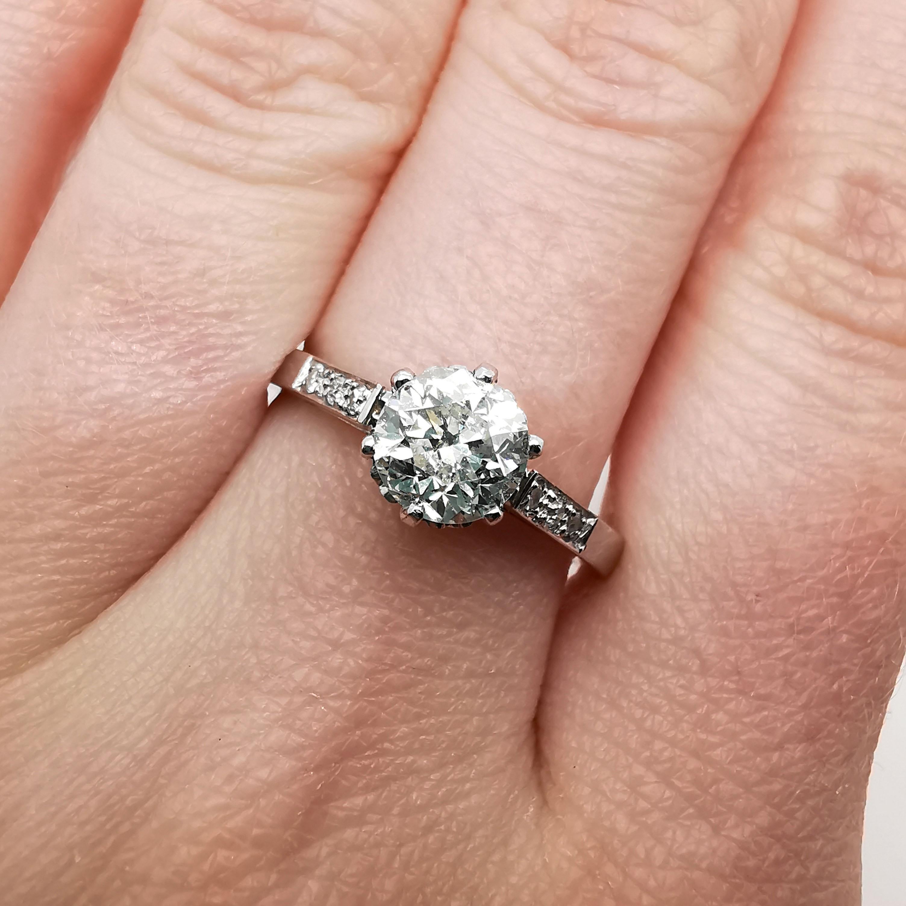 A single stone diamond ring, set with a 1.00 carat, L colour, I1 clarity round brilliant-cut diamond, in a six claw setting, with hearts decorating the collet between the claws, with three small diamonds set in each shoulder, in grain settings,