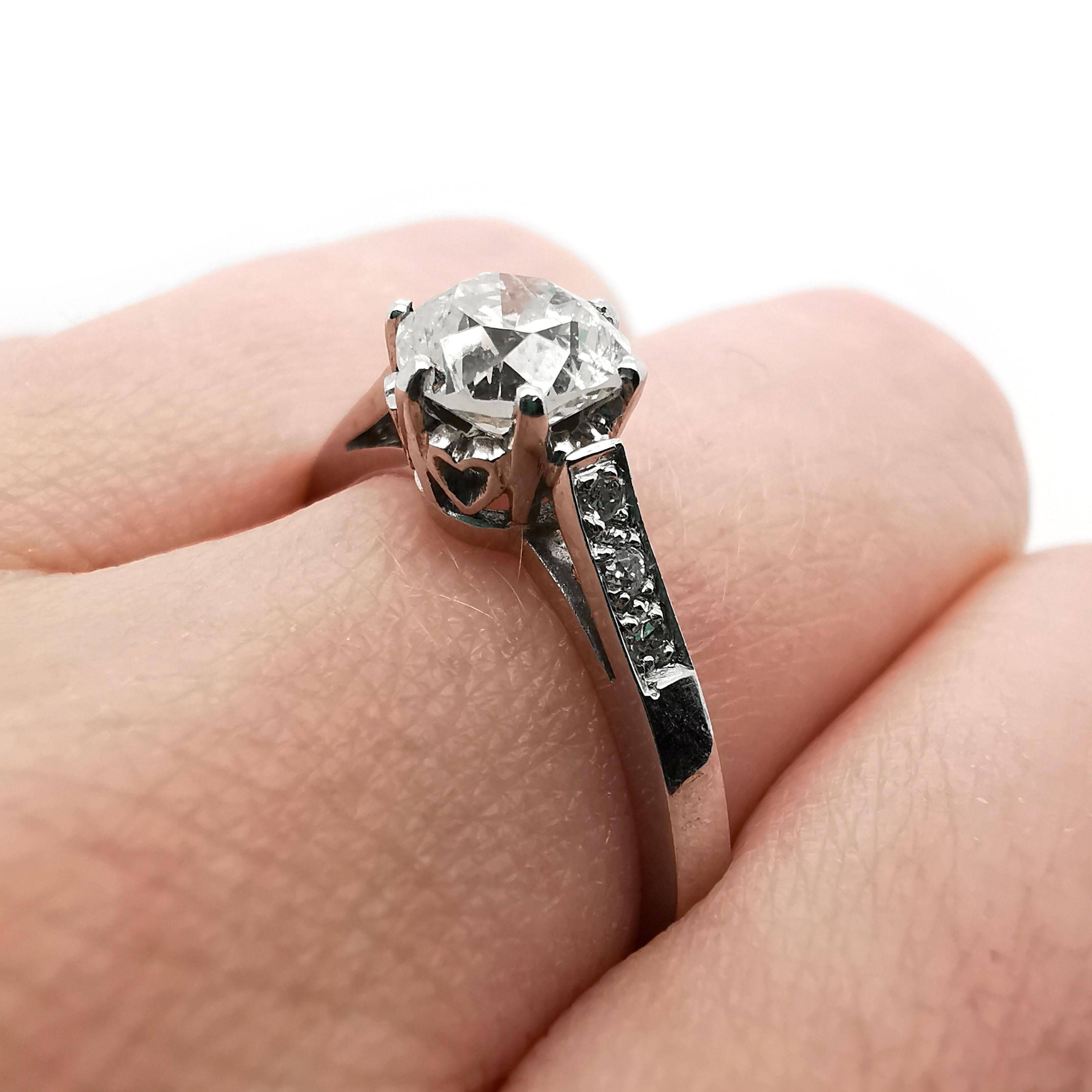 A single stone diamond ring, set with a 1.00 carat, L colour, I1 clarity round brilliant-cut diamond, in a six claw setting, with hearts decorating the collet between the claws, with three small diamonds set in each shoulder, in grain settings,