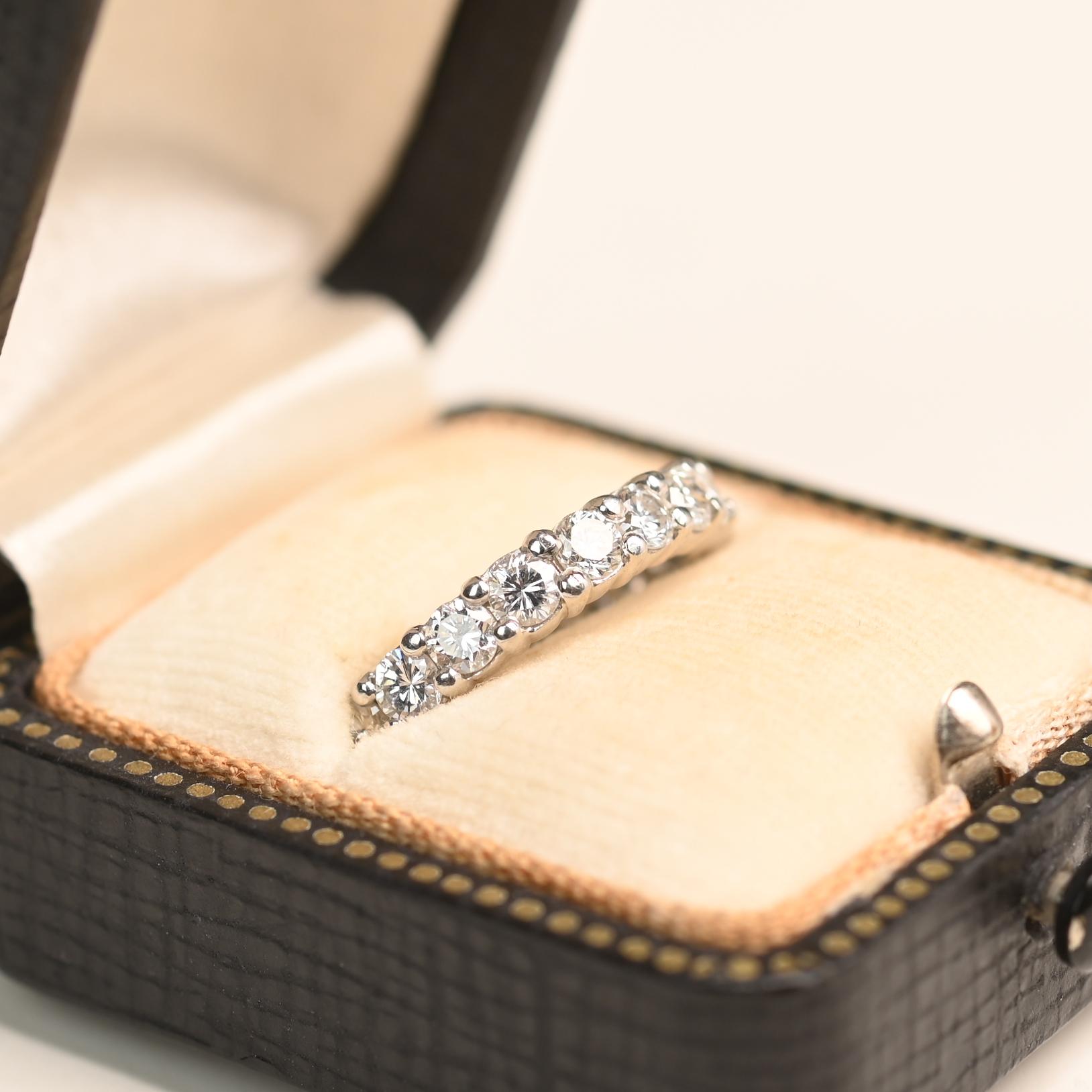 Esta elegante alianza de eternidad presenta una hilera continua de diamantes redondos de talla brillante engastados en garras compartidas. Los diamantes tienen un peso combinado de aproximadamente 2 quilates, ofreciendo un brillo y resplandor