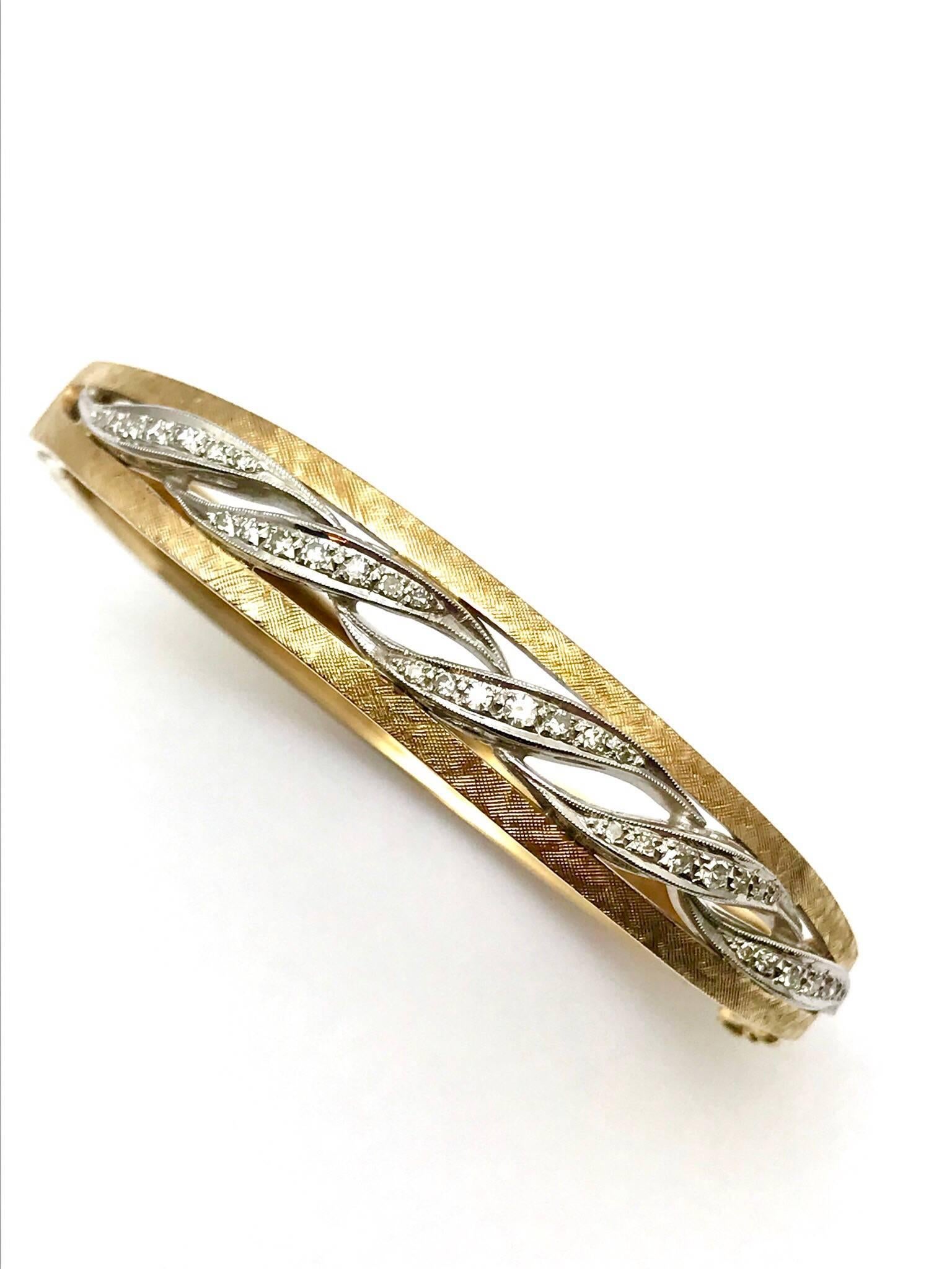 A round brilliant 14 carat white and yellow gold wave bangle bracelet.  The bracelet is designed with a textured yellow gold pattern, containing 35 round brilliant diamonds set in white gold on the top half of the bangle, between the yellow gold. 