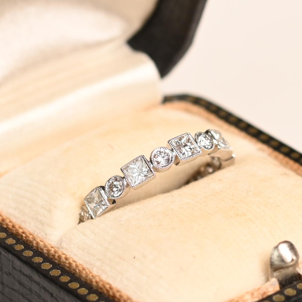 Este exquisito anillo de boda presenta un sofisticado patrón alternado de diamantes redondos talla brillante y talla princesa, cada uno de ellos engastado en bisel de forma segura para lograr un diseño elegante y sin fisuras. Con un peso total