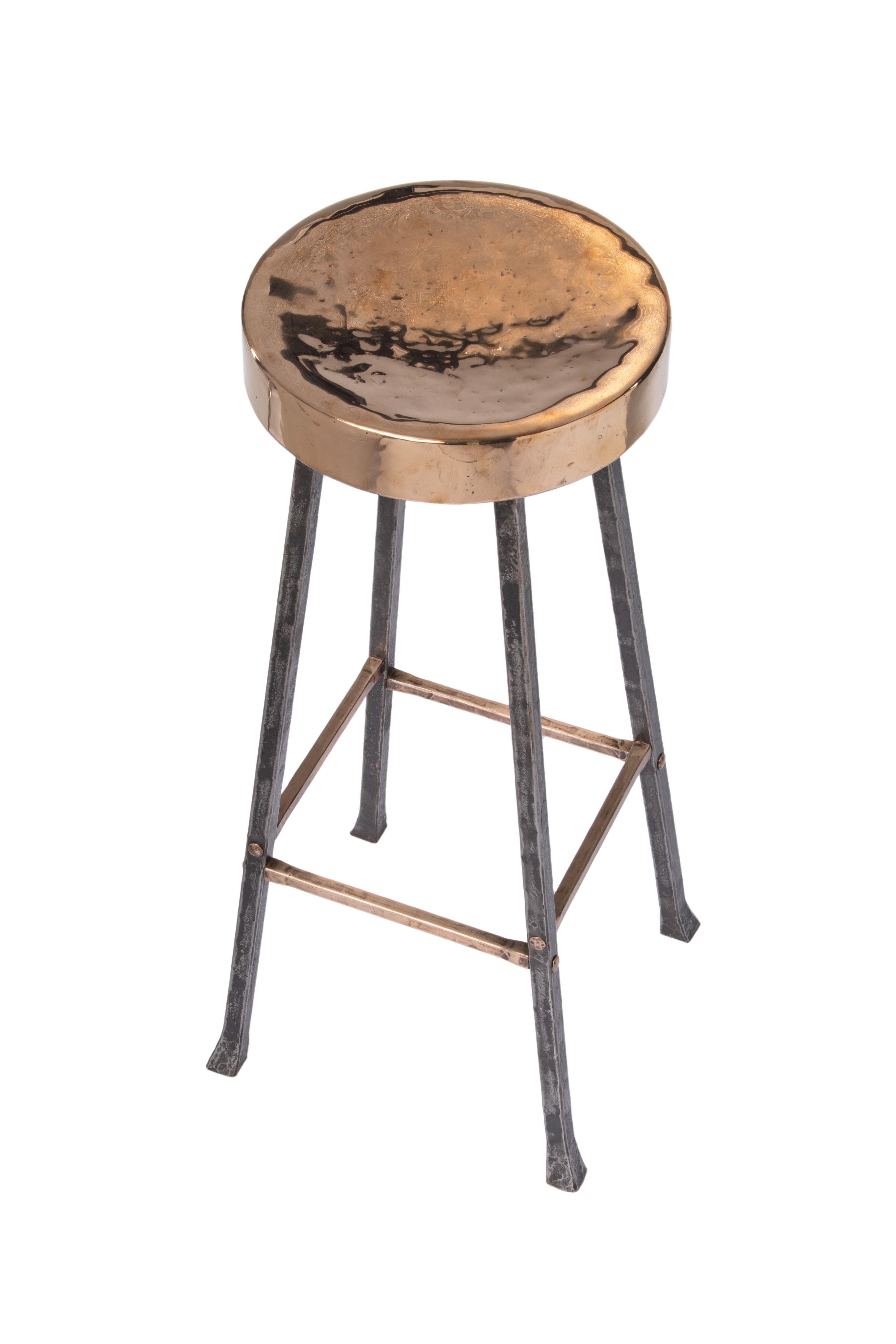 This bronze and steel stool is designed to be paired with a bar. The smooth bronze seat is made from a single piece of bronze surrounding a wood core. The steel legs are forged using traditional joinery techniques and hammered details provide