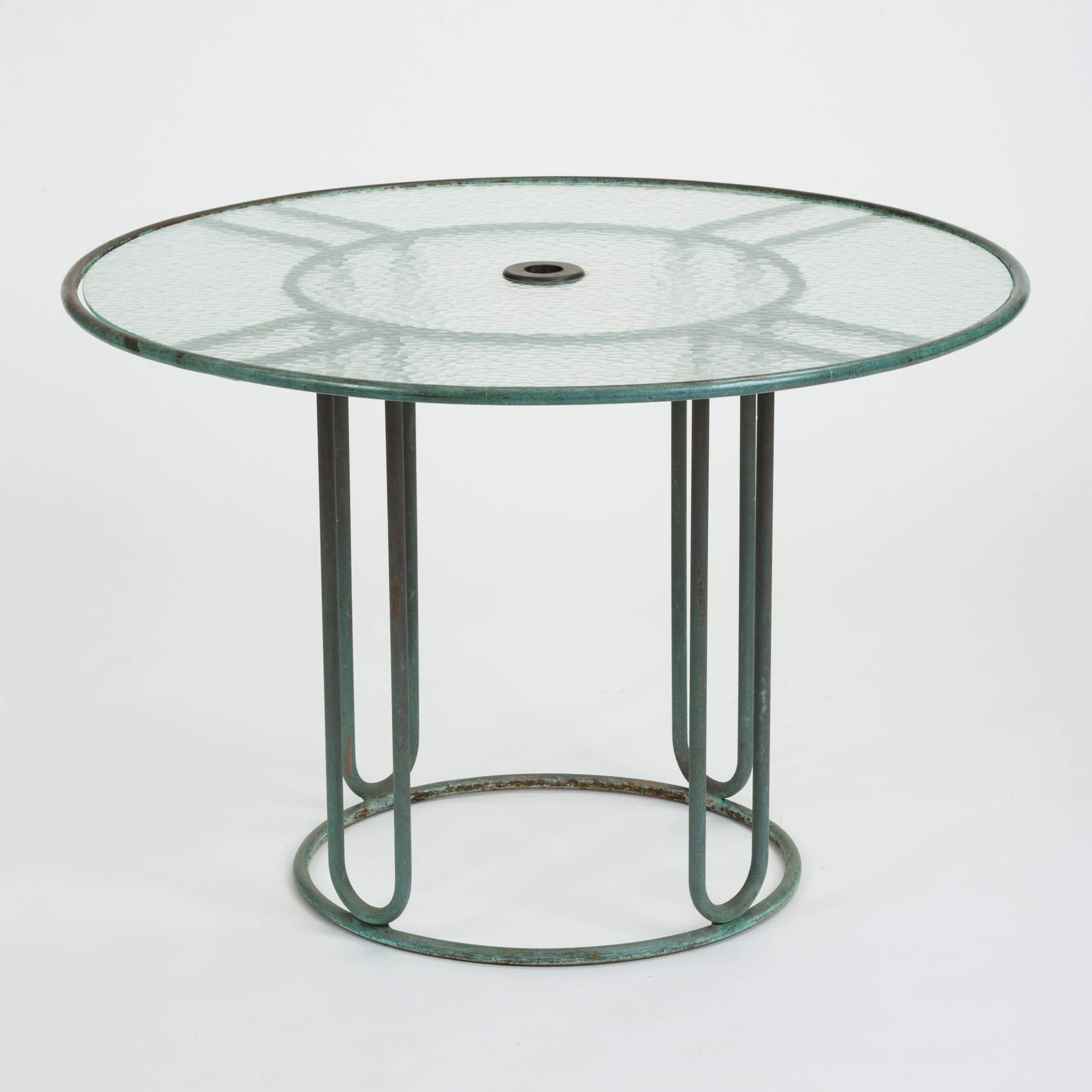 A patio dining table in patinated bronze designed by Walter Lamb and produced by Brown Jordan. The round frame is described by two concentric rings of bronze with radial supports and a circular bronze base. The round tabletop is a single piece of