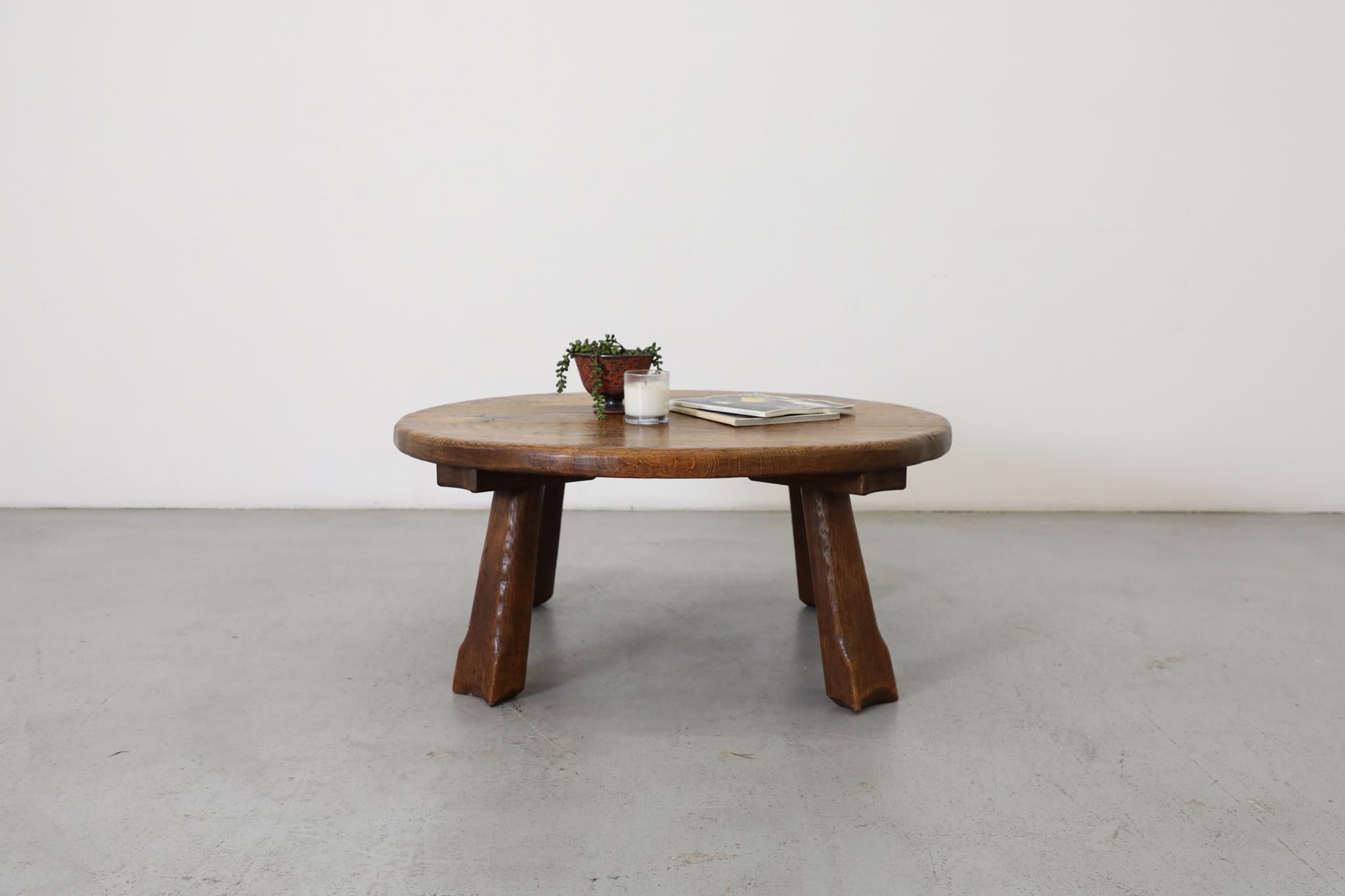 Round Brutalist solid oak coffee or side table with four sturdy angled legs and lovely carved arch detail. A rustically styled coffee table with beautiful grain pattern and natural light and dark wood tones. In original condition with visible wear,