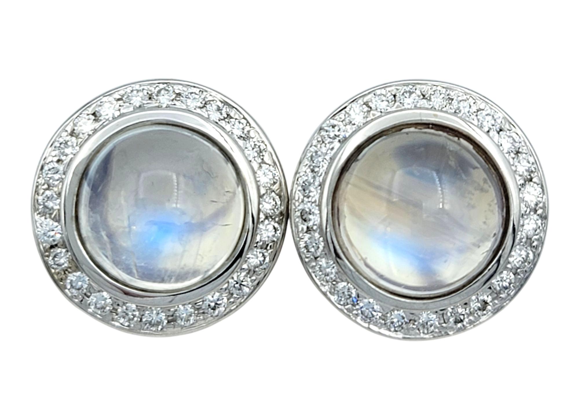 These moonstone and diamond earrings are striking in both design and presence. Each earring showcases a luminous round cabochon moonstone, displaying a range of soft, shifting colors that give them a dreamy, iridescent appeal. The moonstones are