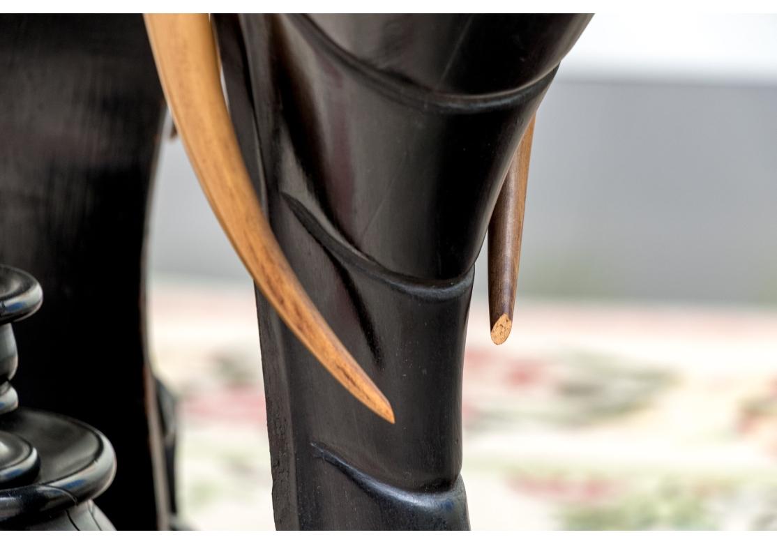 An ebonized side table or pedestal comprised of three well carved elephant heads with decorative bronze mounts. The elephants heads with contrasting carved wood tusks. The elephant heads alternate with bronze classical or mythological figural masks