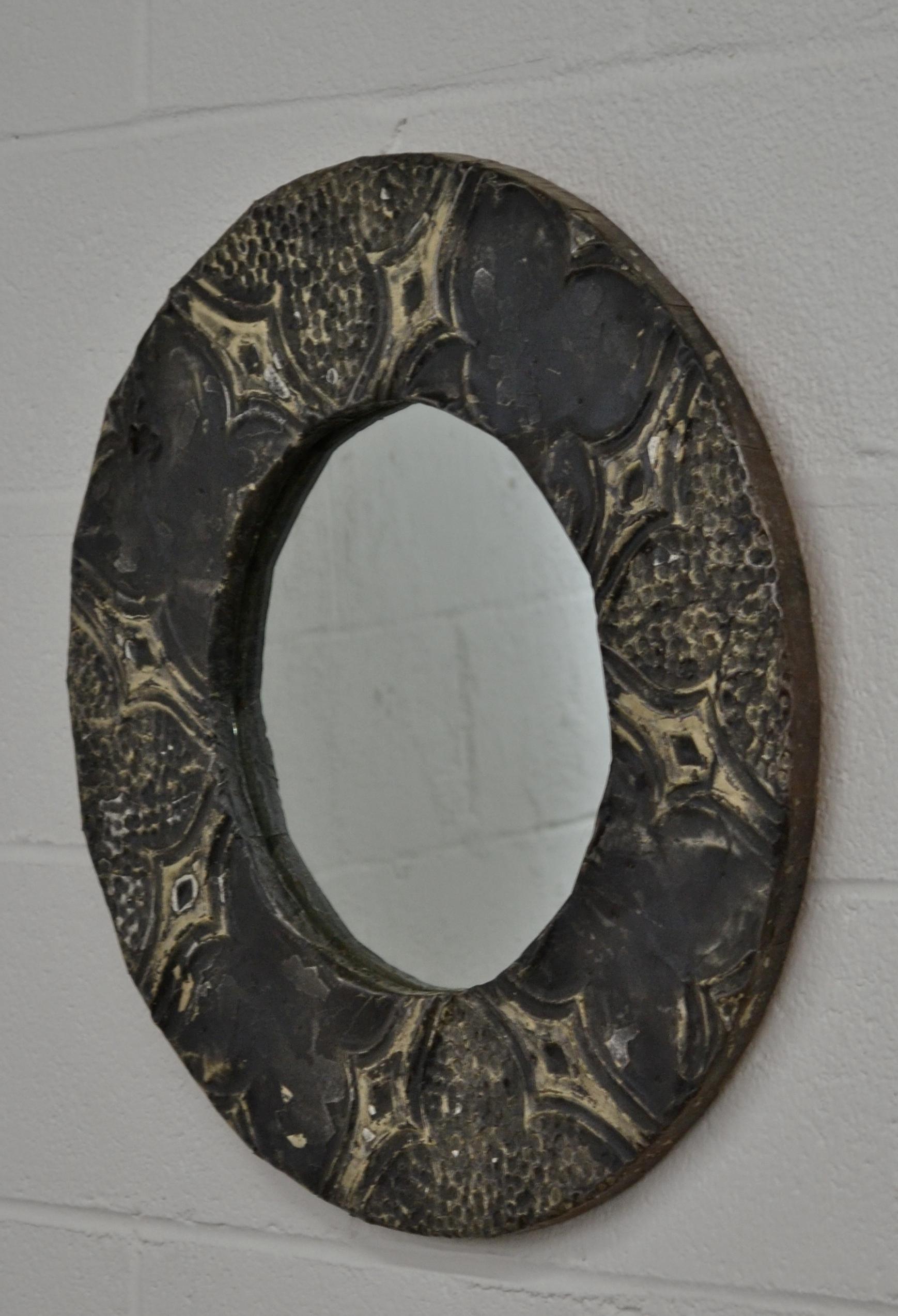 This is a decorative round wall mirror, the frame clad with antique reclaimed ceiling tins in old worn black paint. New glass. This mirror would be perfect for a small powder room or hallway.