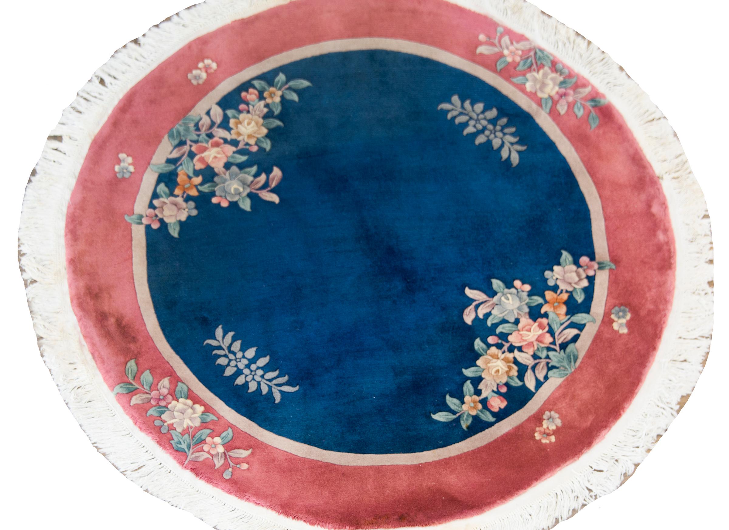 A beautiful early 20th century Chinese Art Deco round rug with a dark indigo field surrounded by a thin taupe stripe and wide burgundy stripe border, overlaid with multi-colored peonies woven in soft pastels.