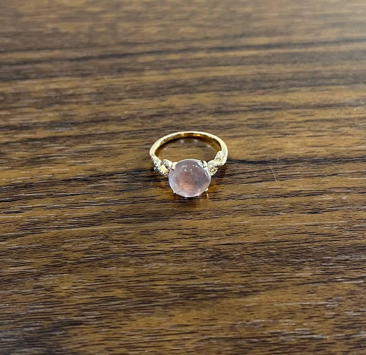 Elegant 14K Gold Ring with Rose Quartz Center Stone. This exquisite ring features a smooth, round-shaped rose quartz set in a 14k gold band. The band is delicately adorned with small, sparkling diamond accents on either side of the center stone. The