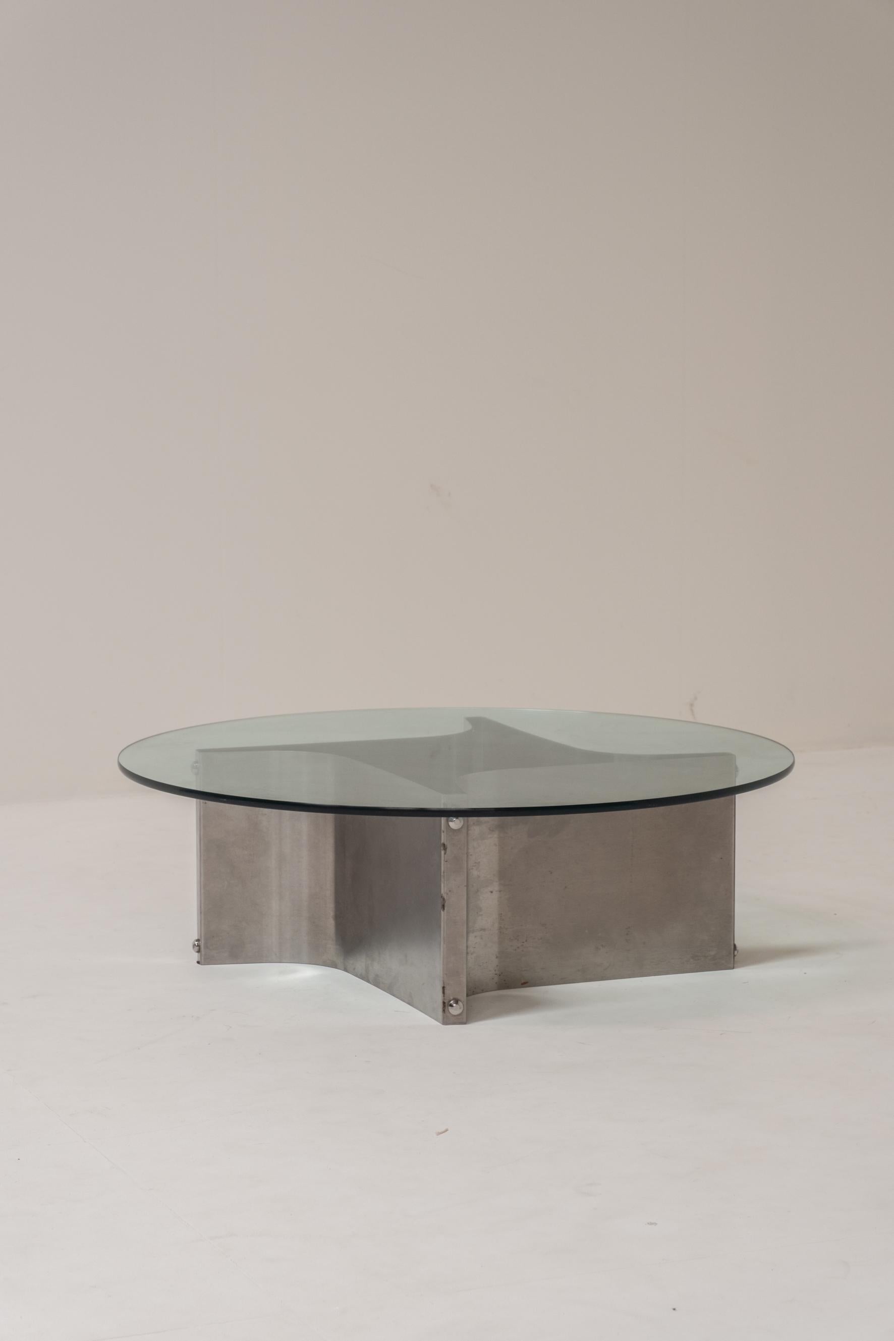 Sculptural coffee table featuring a thick circular glass top resting on François Monnet’s signature base composed of four elegantly curved stainless-steel panels, joined together with exposed industrial bolts. This distinctive construction creates a
