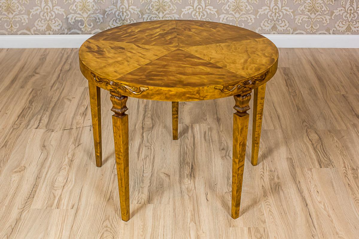 We present you this small table in birchen veneer.
The round tabletop is supported on four legs in the shape of an inverted pyramid.
Moreover, the legs are finished with the heads that look like tulips.
On their line, at the apron section, there