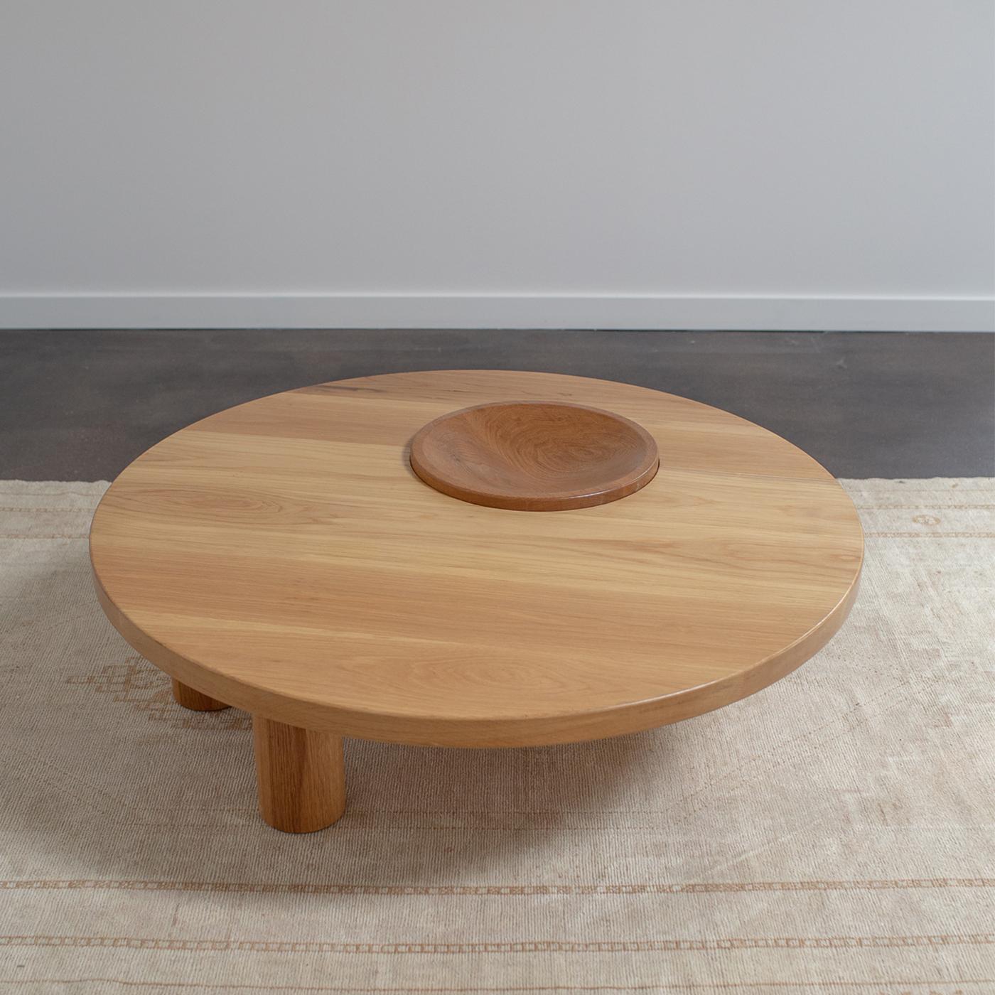 A three-legged solid oak round coffee table with built in bowl. The large leg is stationary with two smaller moveable legs.