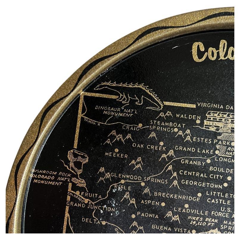 A Mid-Century Modern Colorado metal serving tray decorated with the Columbine flower and the outline of Colorado, its attractions, and towns. A great addition to your barware, this tray is black, with gold accents, a small lip, and purple and green