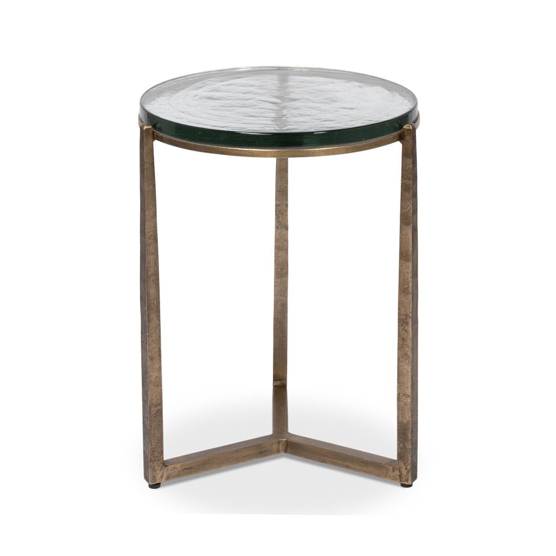 Dieses exquisite Stück verfügt über einen handgeschmiedeten Eisensockel in gealterter Messingausführung, der einen Hauch von Vintage-Eleganz vermittelt und gleichzeitig eine schlichte, moderne Ästhetik bewahrt. Die Gussglasplatte mit ihrer