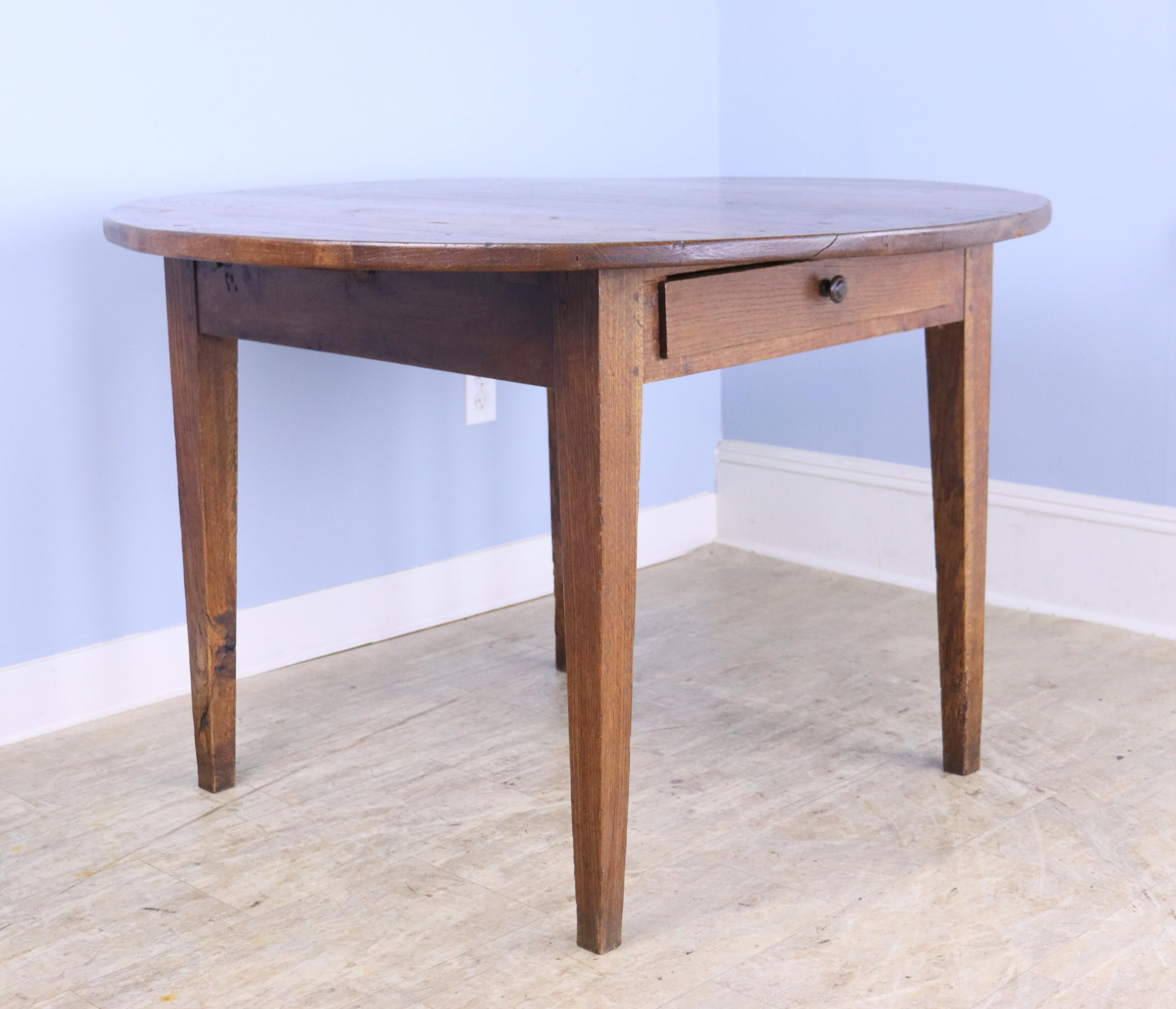 An antique thick topped breakfast farm table from France. Made of oak with rich color and patina.  Very good for small dining table. Classic tapered legs and one roomy drawer. Note that the top is not a perfect circle (there are differences of up to