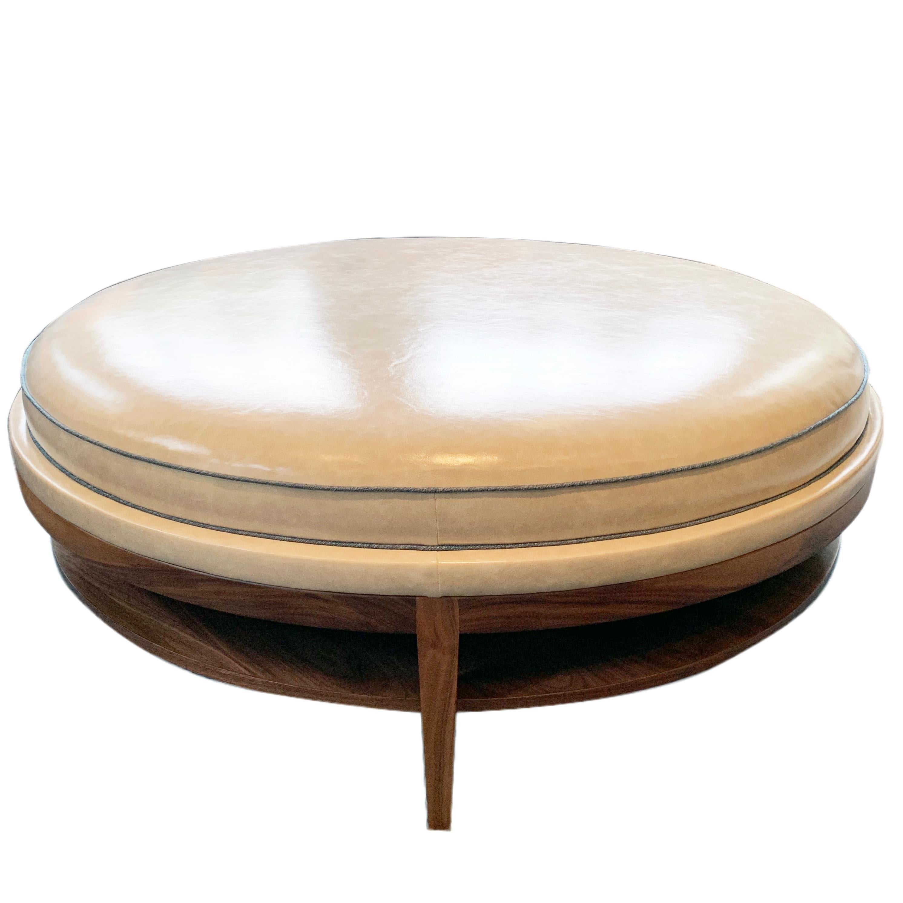 The Donatella coffee table is a Mid-Century Modern inspired design with fashionable flair. The base, featuring a shelf for storage and tapered leg accents, is handcrafted with walnut wood and finished with a honey stain. The round cushioned top is
