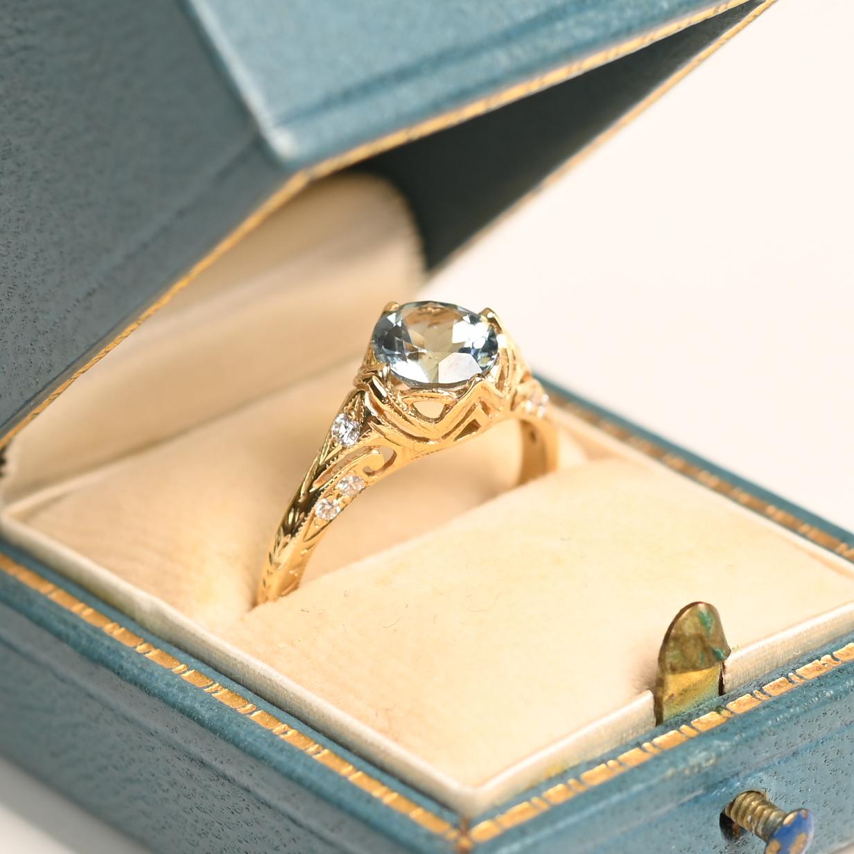 Cette bague exquise met en valeur une aigue-marine ronde d'environ 0,90 carat, solidement sertie dans de délicates pinces. La teinte froide et sereine de la pierre précieuse contraste magnifiquement avec la chaleur de la monture en or jaune 18