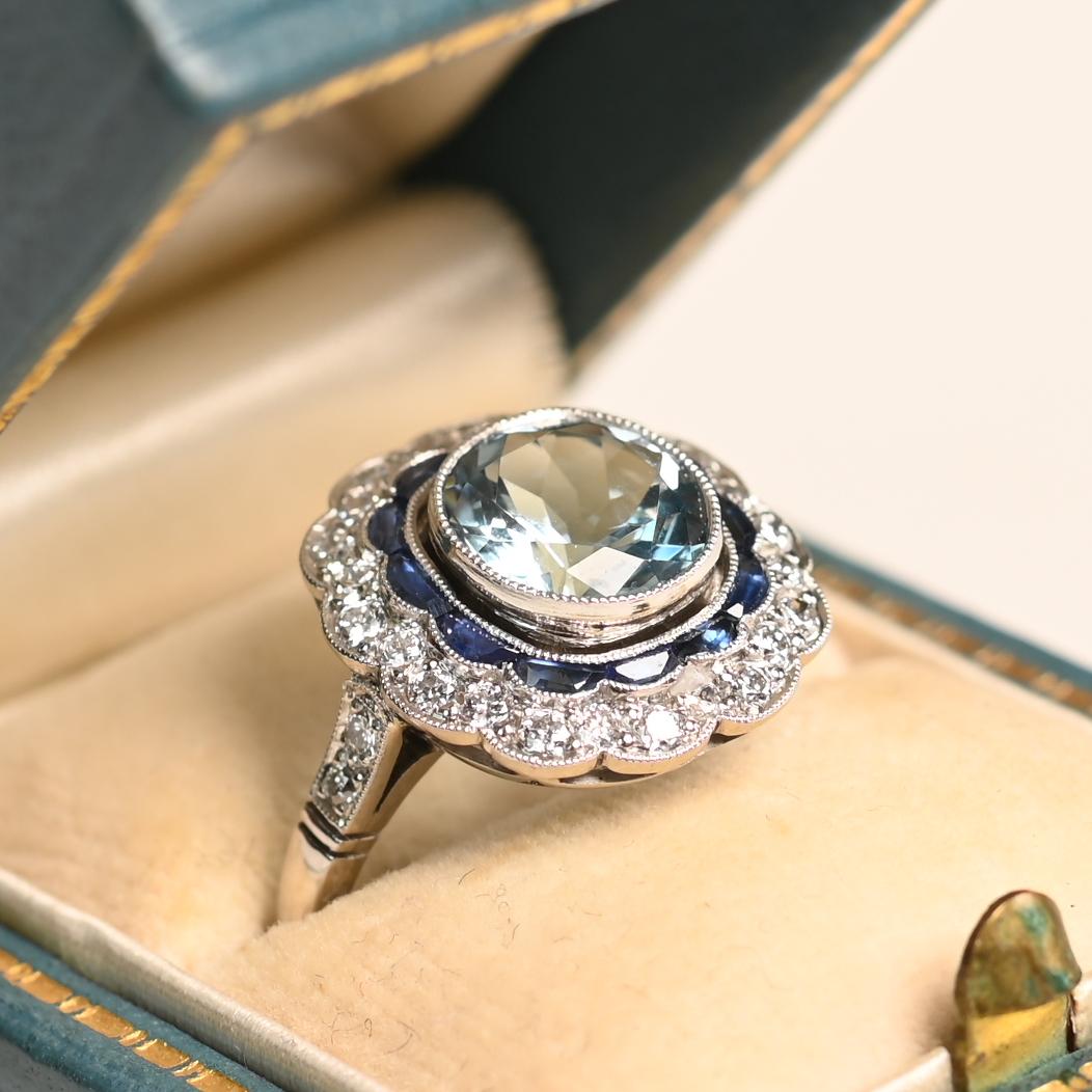 Cette bague exquise est ornée d'une superbe aigue-marine de taille ronde d'environ 1,60 carat, sertie en chaton pour une esthétique à la fois raffinée et contemporaine. L'aigue-marine est entourée d'un halo de saphirs, disposés avec art dans un