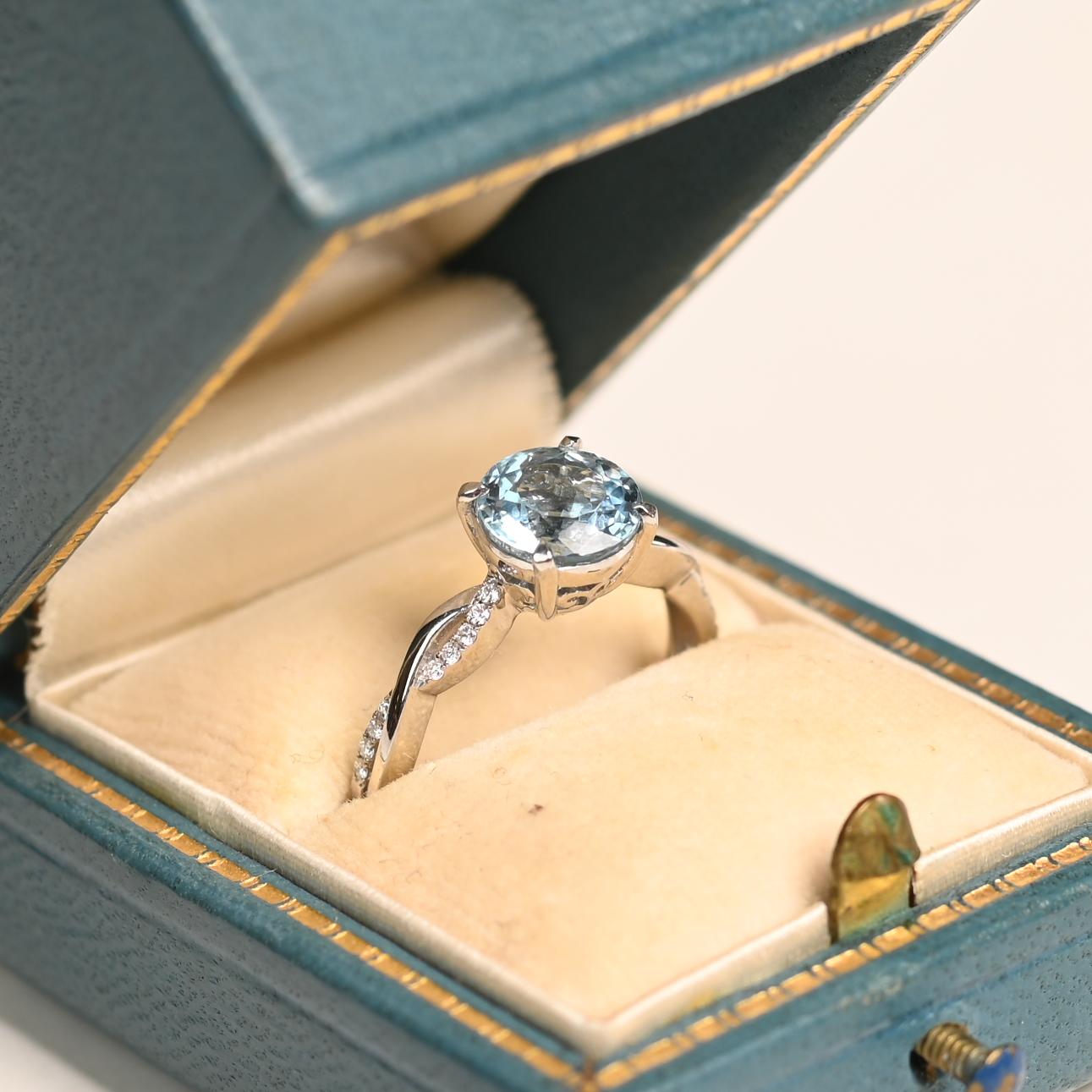 Este exquisito anillo exhibe una impresionante gema de aguamarina natural de aprox. 1,3 quilates, magistralmente tallada en una brillante forma redonda que irradia claridad y serenidad. La piedra central está sujeta con seguridad en un refinado