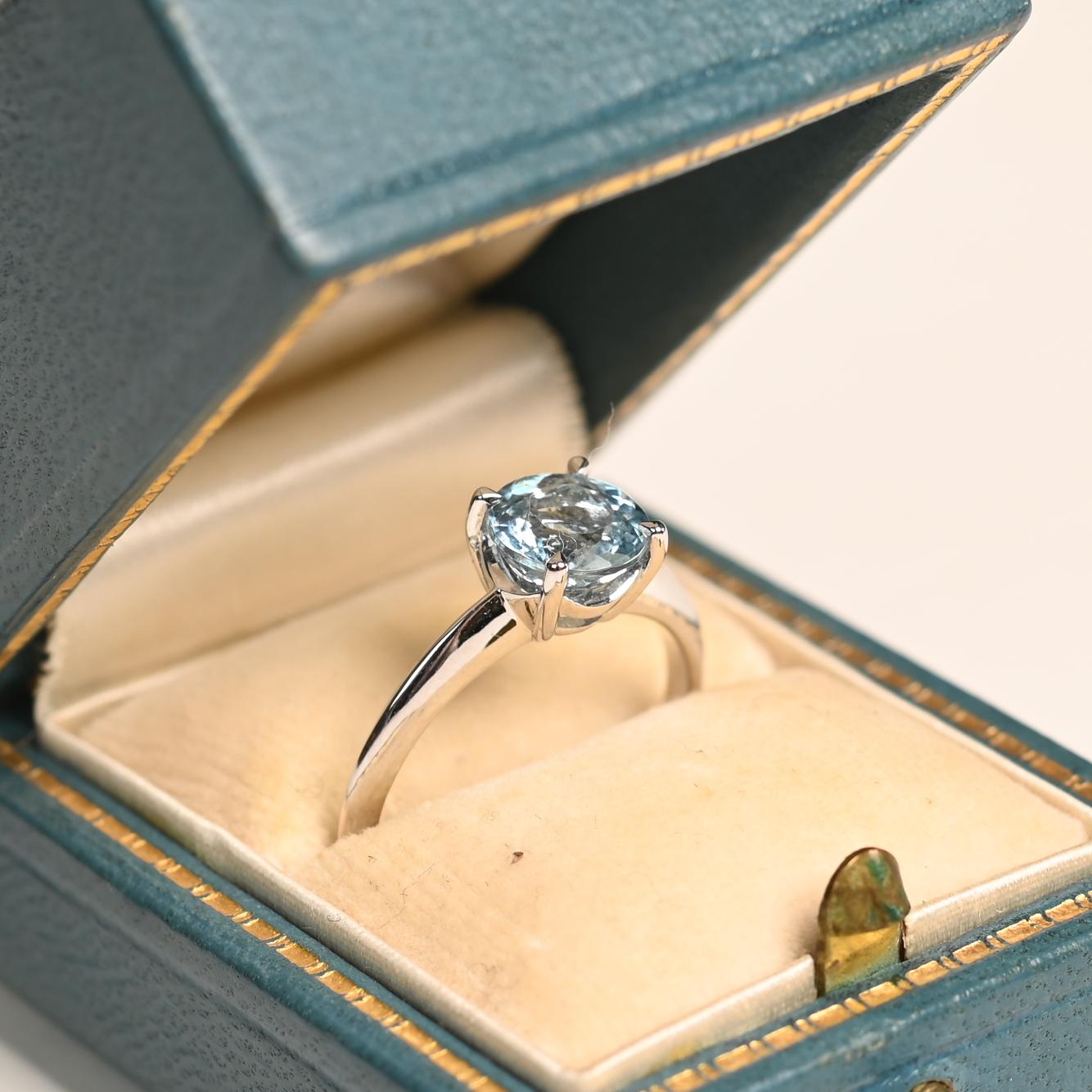 Cette bague de fiançailles solitaire est ornée d'une aigue-marine naturelle de taille ronde d'environ 1,10 carat. L'aigue-marine, réputée pour sa clarté et sa brillance, est montée en platine, un métal apprécié pour sa durabilité et son éclat