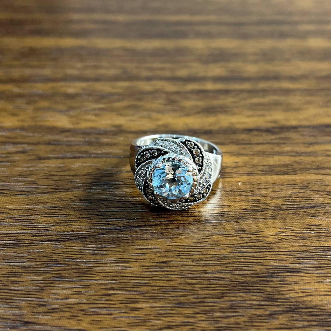 Cette pièce exquise présente une topaze bleue primaire ronde, magnifiquement sertie dans un motif détaillé. La bague présente des motifs complexes avec des pierres secondaires d'une couleur blanche saisissante, ajoutant de la profondeur et de la