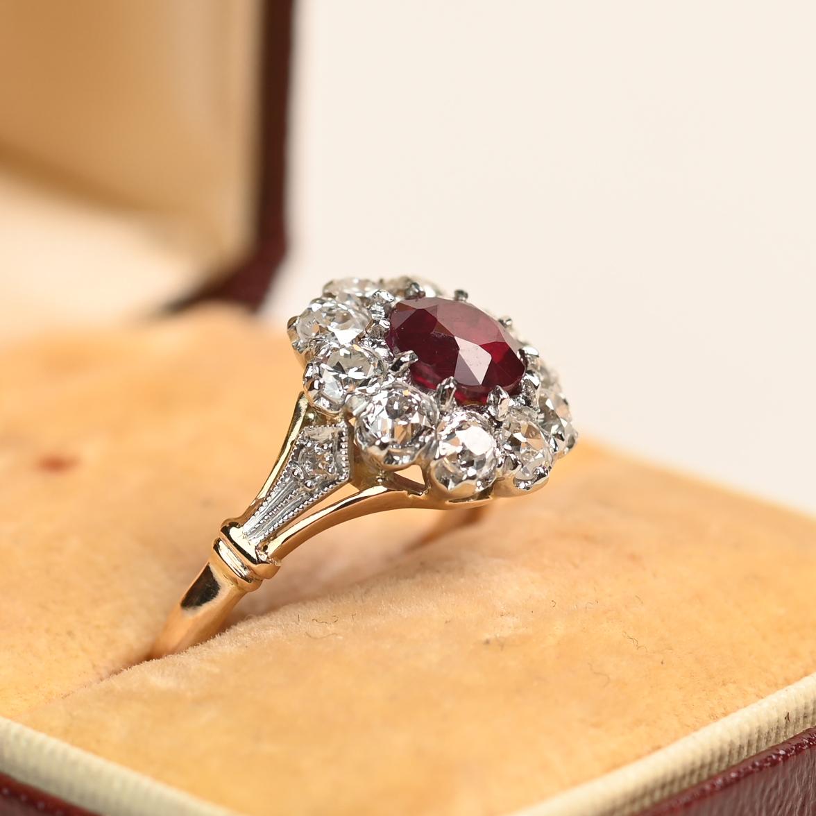 This exquisite ring centers an approximately 0.7-carat round ruby, securely held in a prong setting. Surrounding the vivid red gemstone is a cluster of old European cut diamonds with a total weight of approximately 0.8 carats. The shoulders showcase