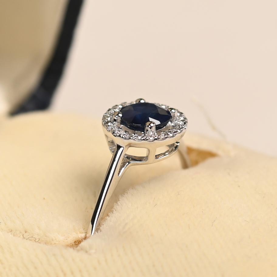 Este elegante anillo exhibe un vibrante zafiro redondo de aproximadamente 0,50 quilates, engarzado en una clásica garra. Alrededor de la piedra central hay un halo resplandeciente de diamantes redondos, con un peso combinado de aproximadamente 0,07