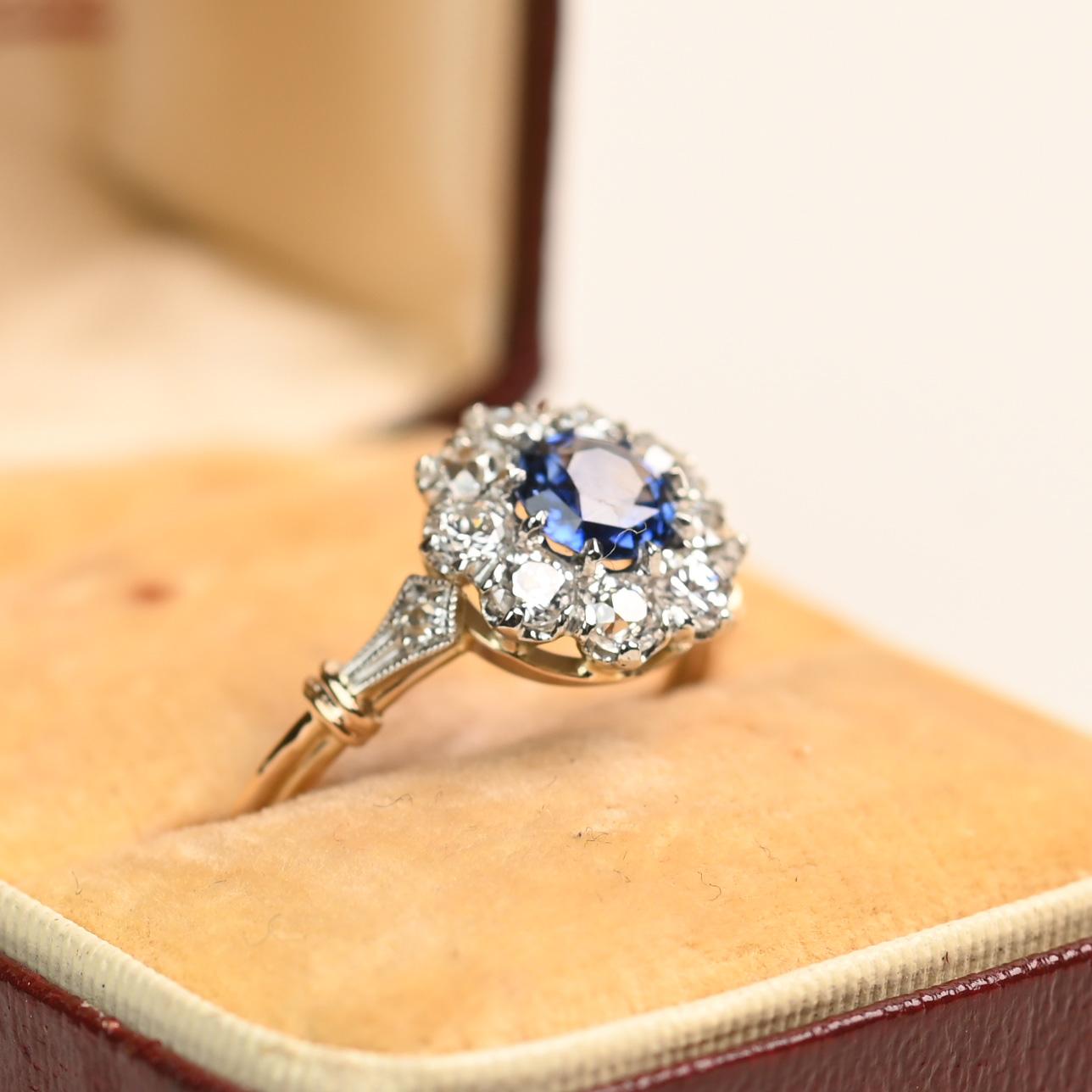 Ein charmanter, von Blumen inspirierter Ring, in dessen Zentrum ein runder Saphir von etwa 0,7 Karat steht, der sicher in einer Zackenfassung gehalten wird. Um das leuchtend blaue Zentrum herum sind Diamanten im alten europäischen Schliff